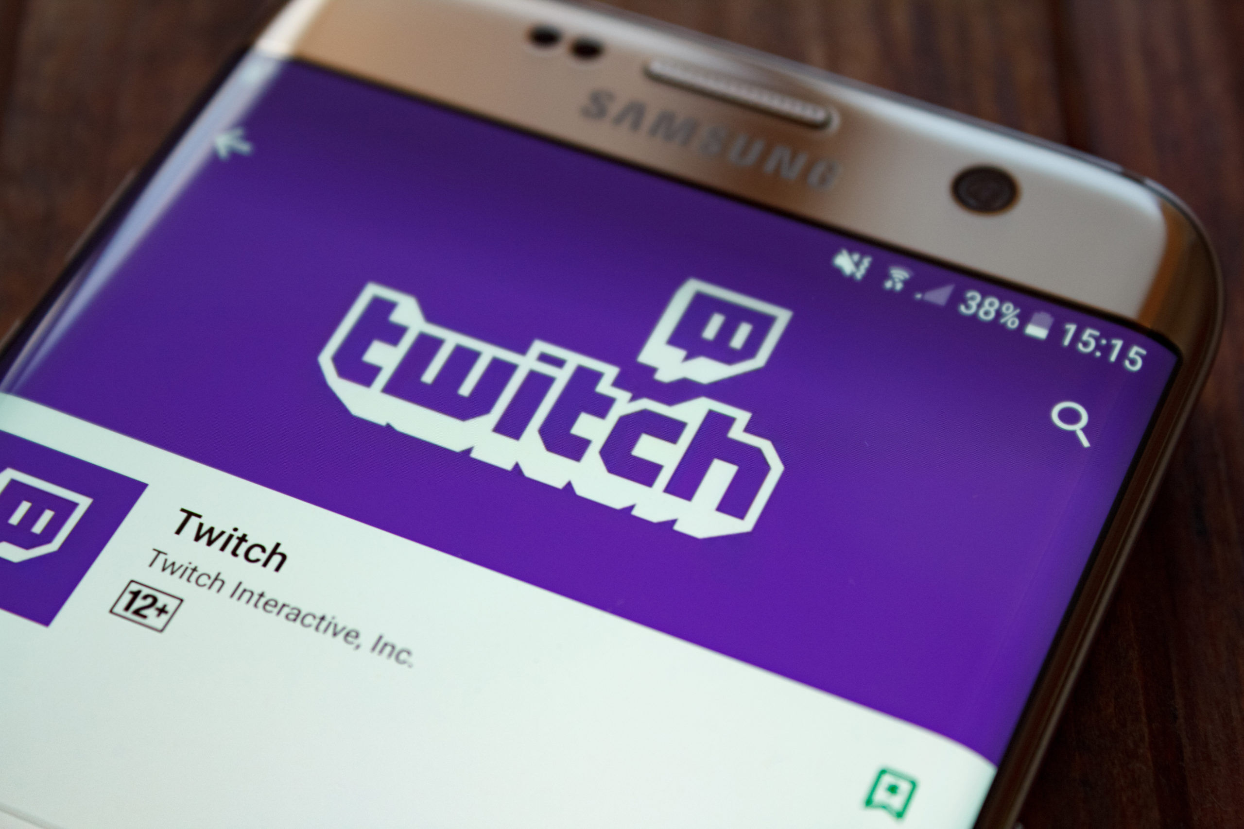 Twitch logo on smartphone screen on wooden background.