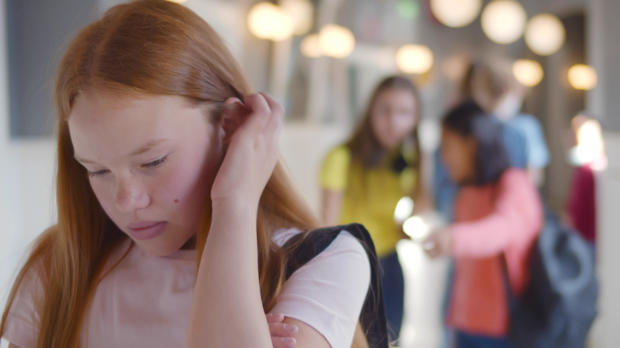 Teen schoolgirl being bullied by group of students in high school. Portrait of depressed female pupil standing in corridor with mean girls gossiping and laughing at her on blurred background