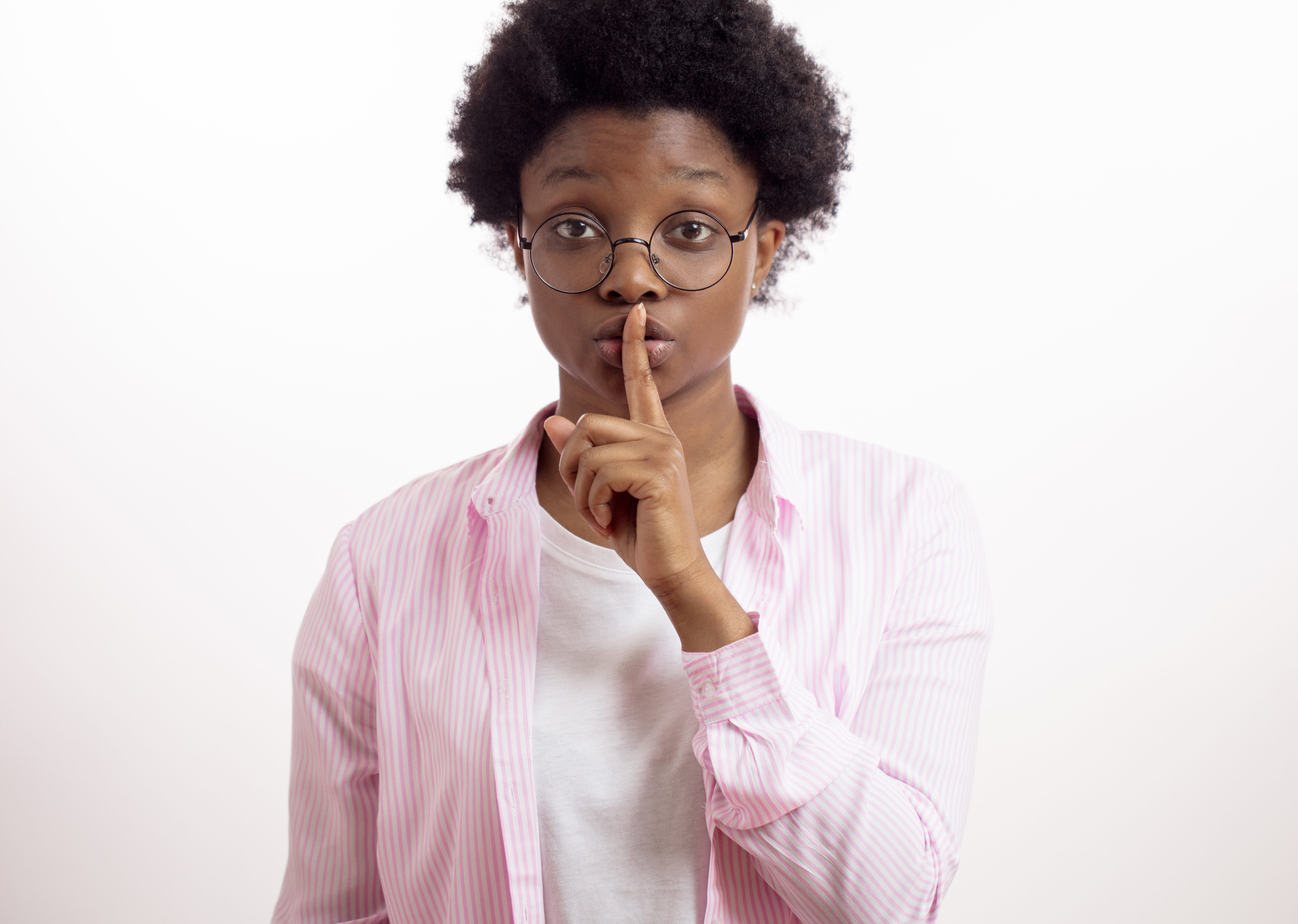 Black woman in pink shirt with a finger on her lips, signaling for silence, to be quiet