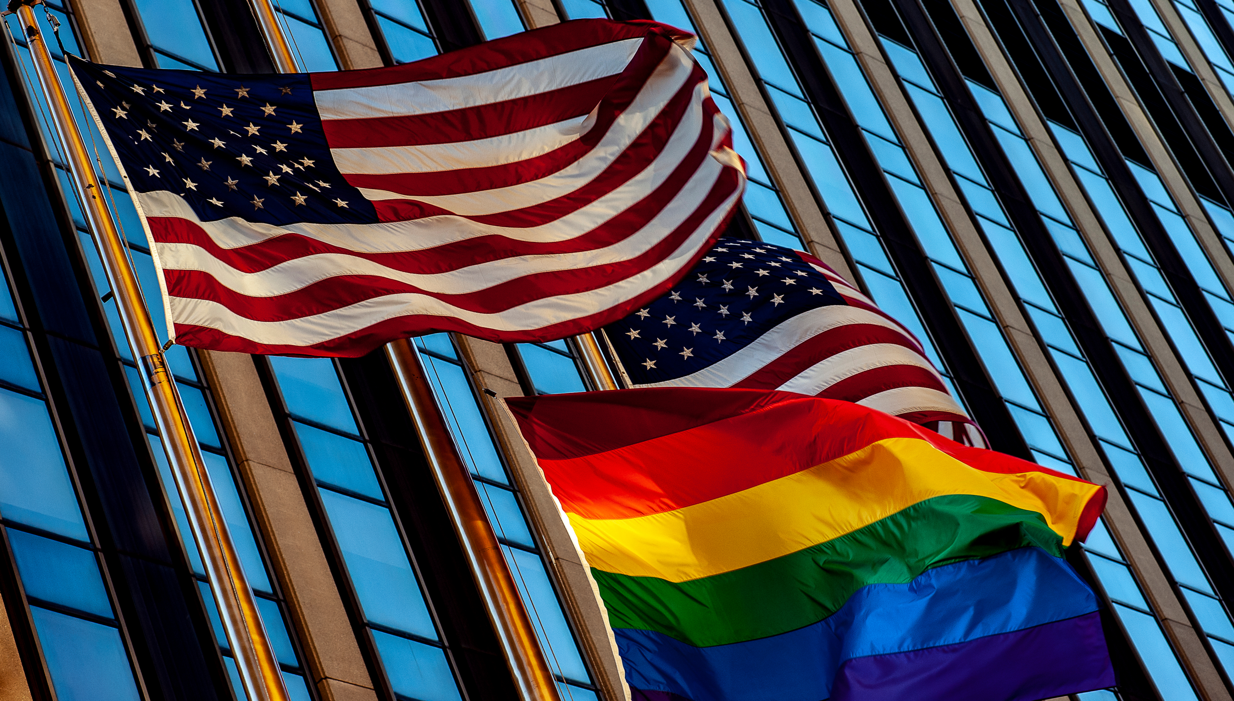 Two American flags waving just above a Pride flag