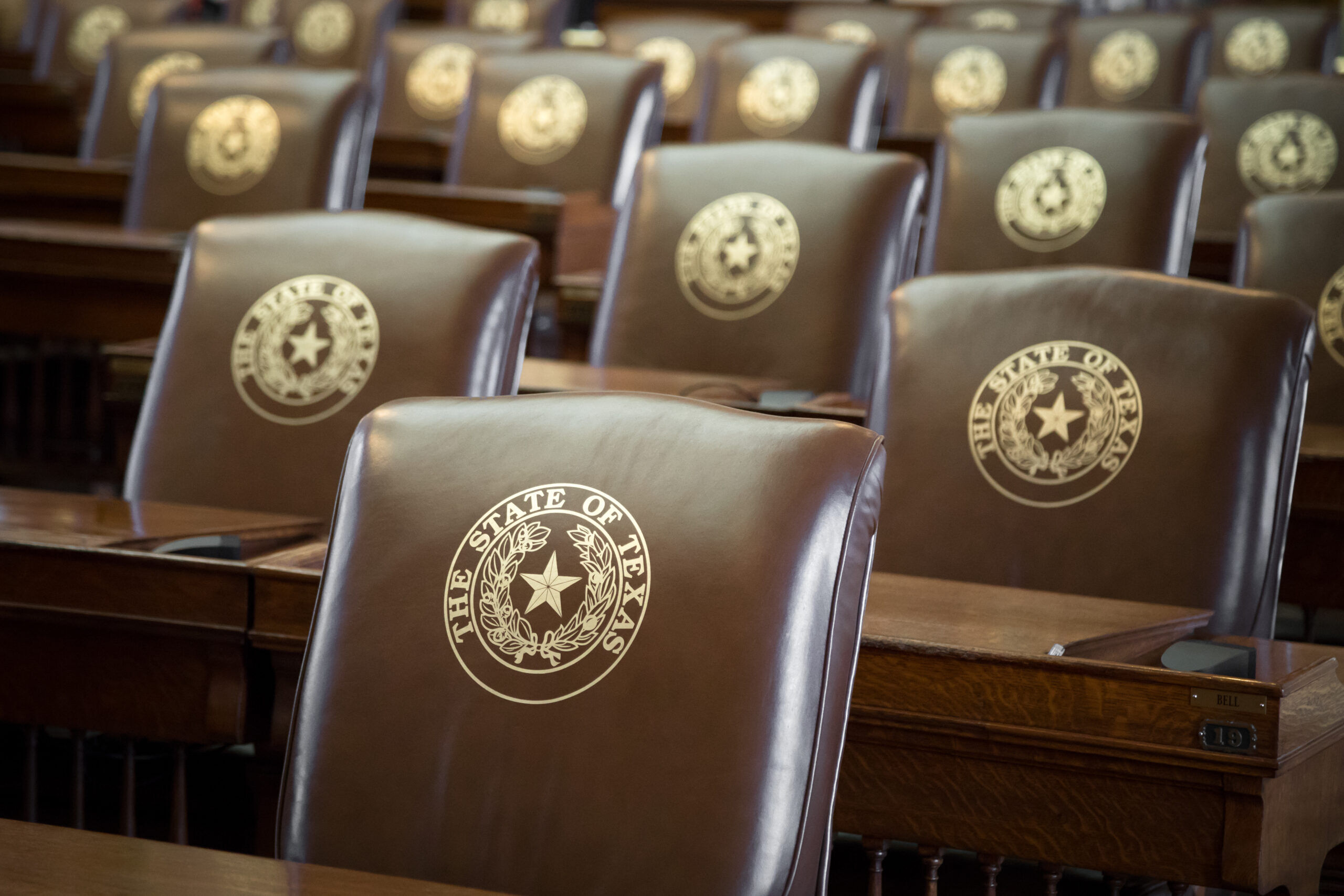 Rows of leather seats, with gold embossed The State of Texas and Lone Star seal, in the House of Representatives chambers at the capitol building