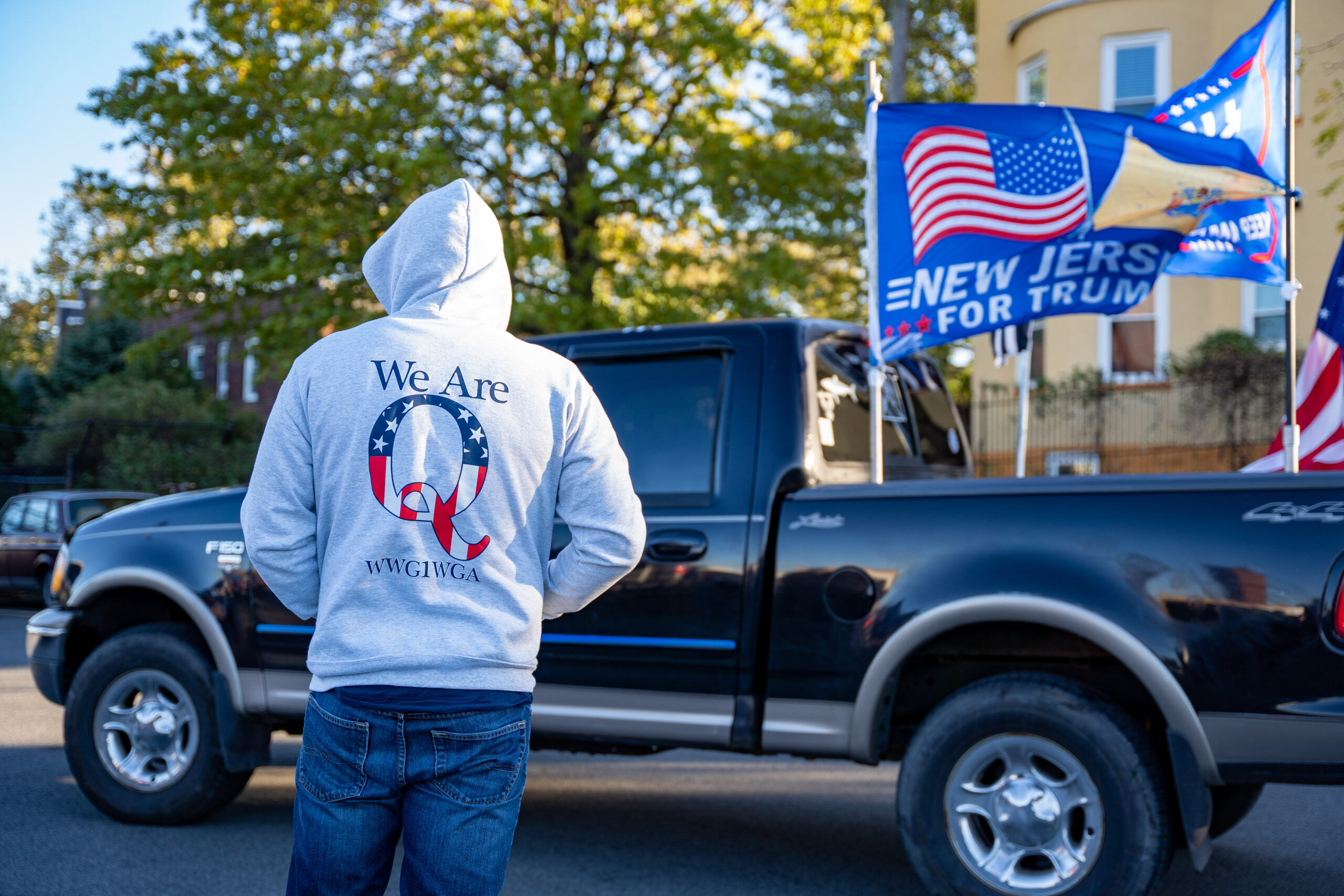 Weehawken, New Jersey, USA - November 2nd, 2020 - Day Before Election Day Trump Rally - Hooded man wearing a Qanon sweatshirt at Trump Rally with Truck and Flags in front of him .