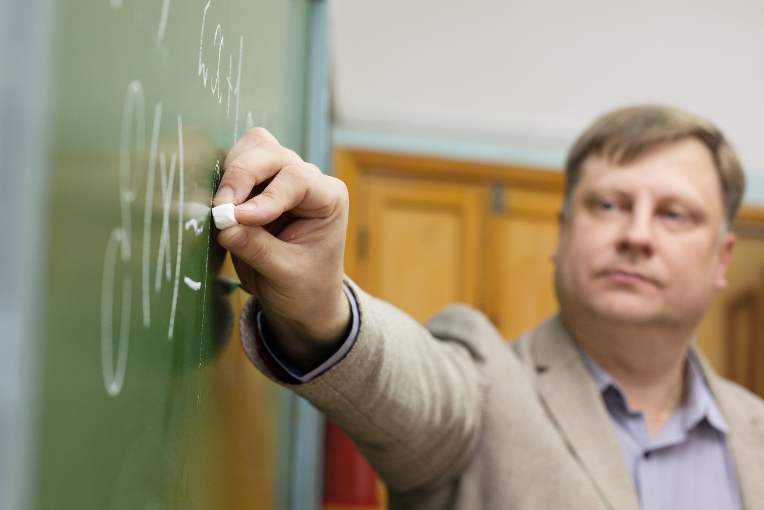 Professor-teacher in classroom at the blackboard writes formulas for students.
