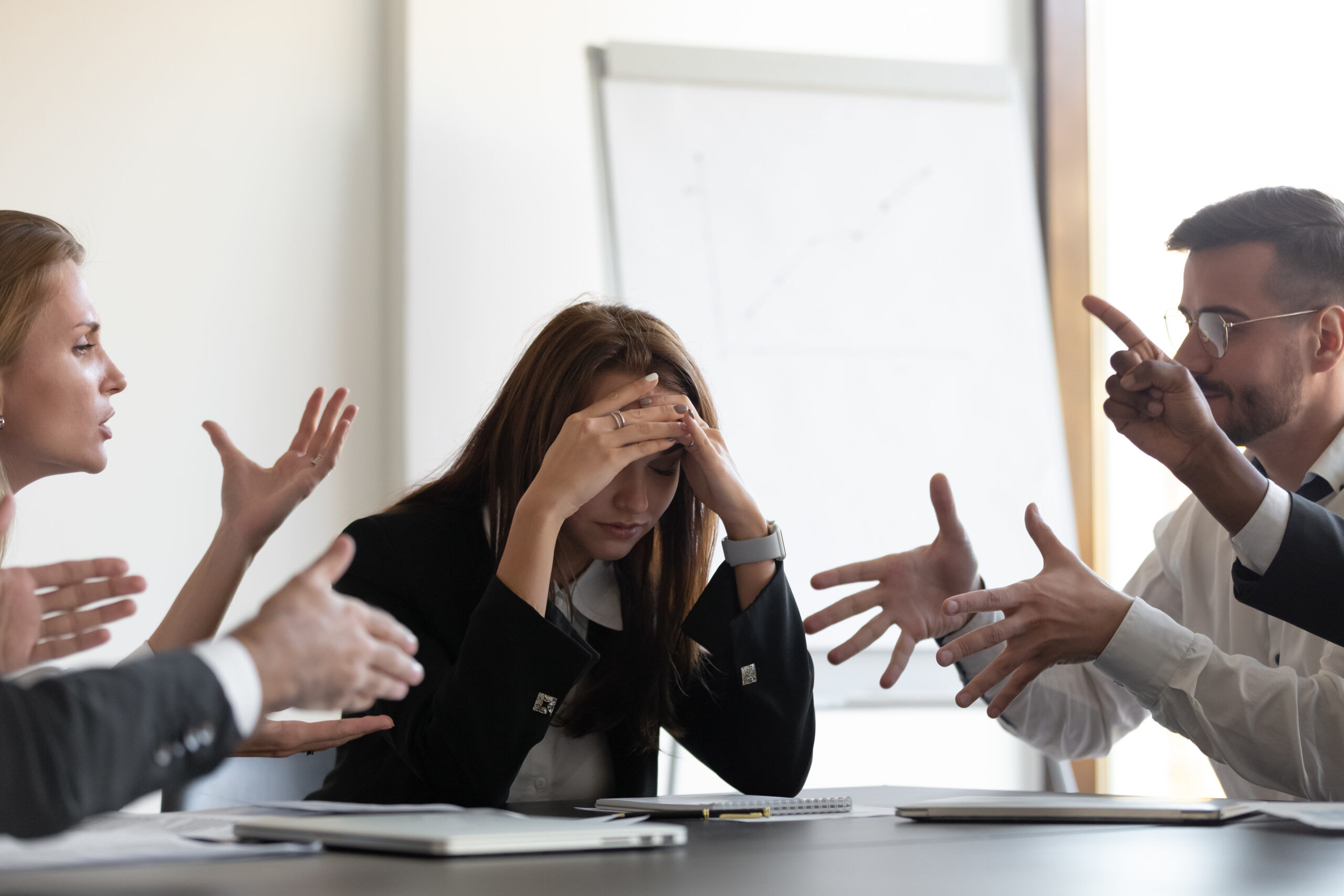 Frustrated millennial female worker sitting at table with colleagues, felling tired of working quarreling at business meeting.