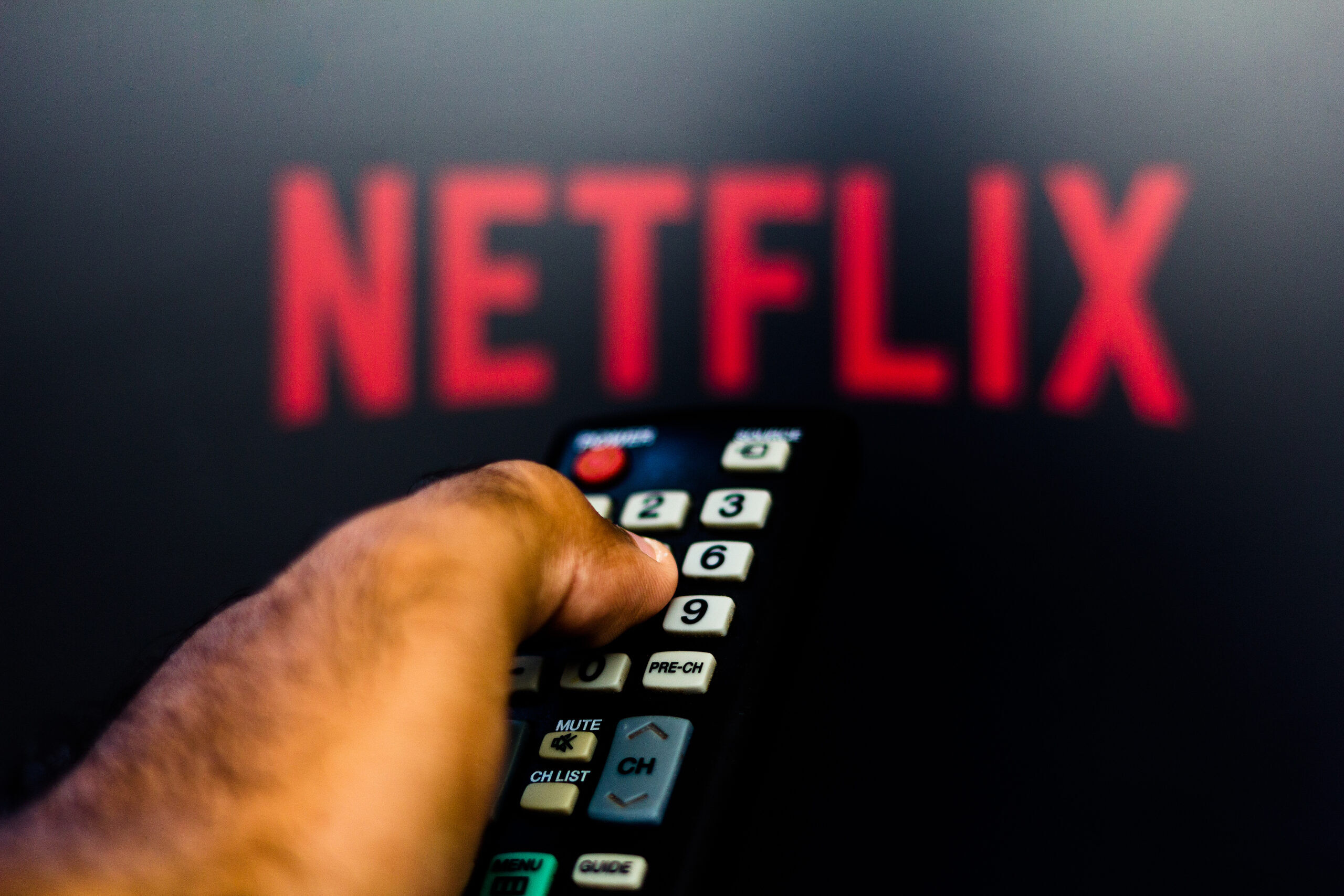 Man with TV remote control in hand and Netflix logo in background.