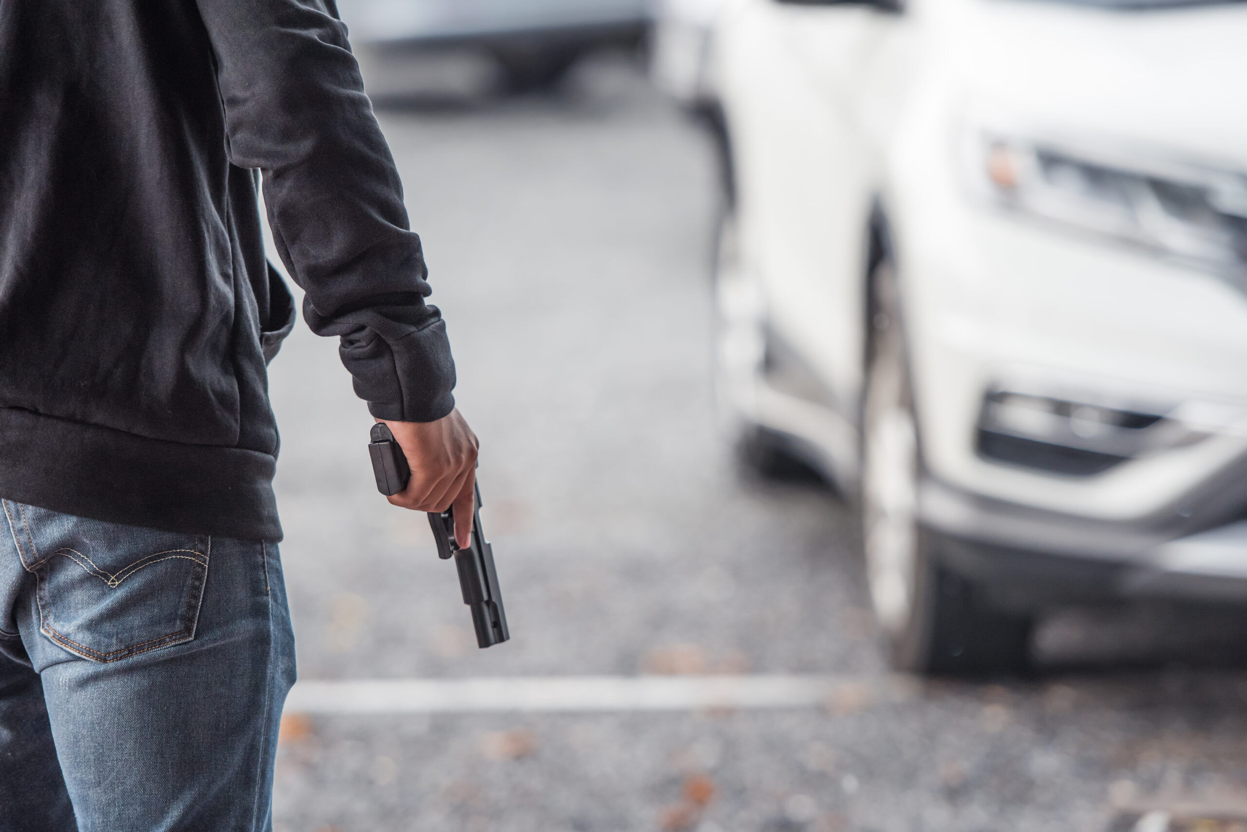 Back view of man holding a gun near a car