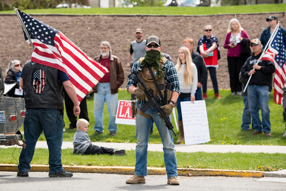 A Montana militia member stands with a gun near a child. The man was protesting coronavirus prevention measures outside the state Capitol building.