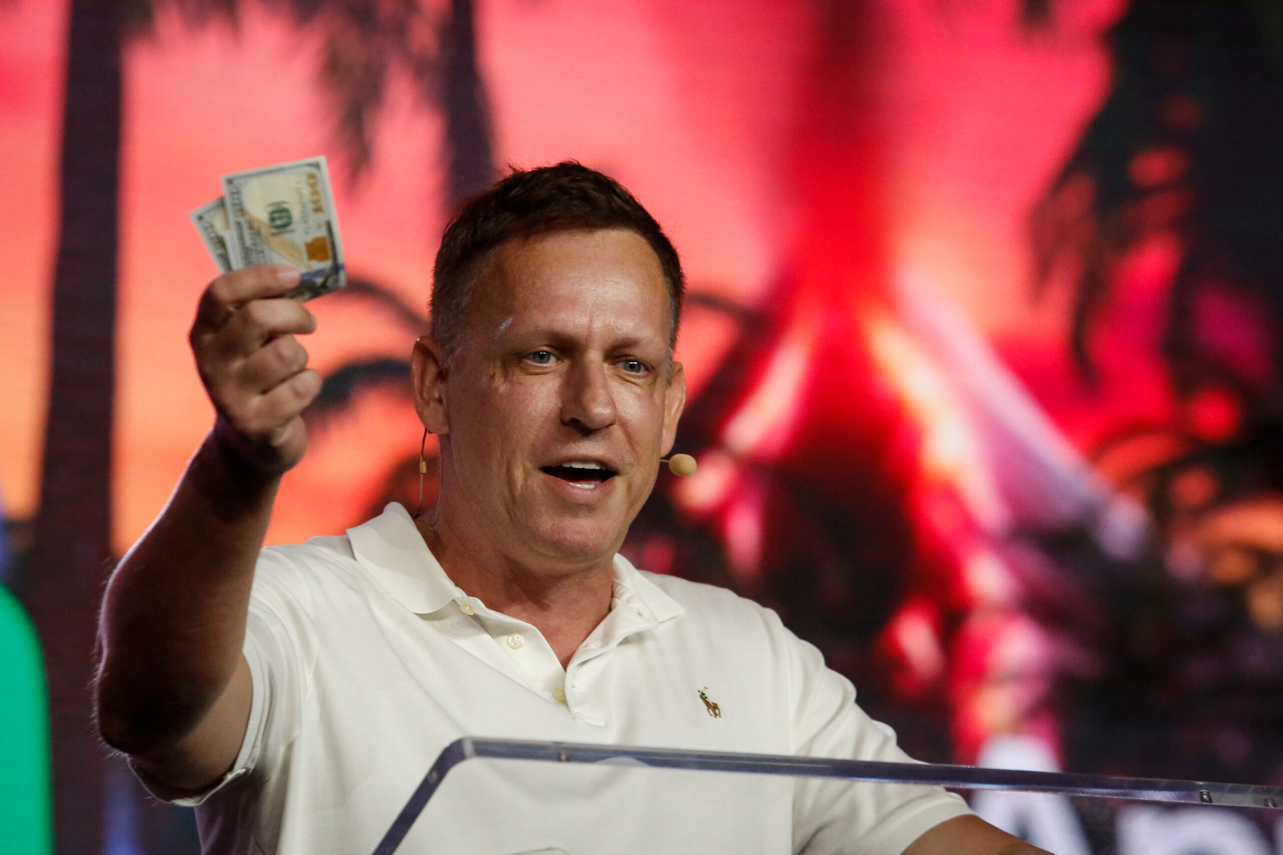 MIAMI, FLORIDA - APRIL 7: Peter Thiel, co-founder of PayPal, Palantir Technologies, and Founders Fund, holds hundred dollar bills as he speaks during the Bitcoin 2022 Conference at Miami Beach Convention Center on April 7, 2022 in Miami, Florida. The worlds largest bitcoin conference runs from April 6-9, expecting over 30,000 people in attendance and over 7 million live stream viewers worldwide.(Photo by Marco Bello/Getty Images)
