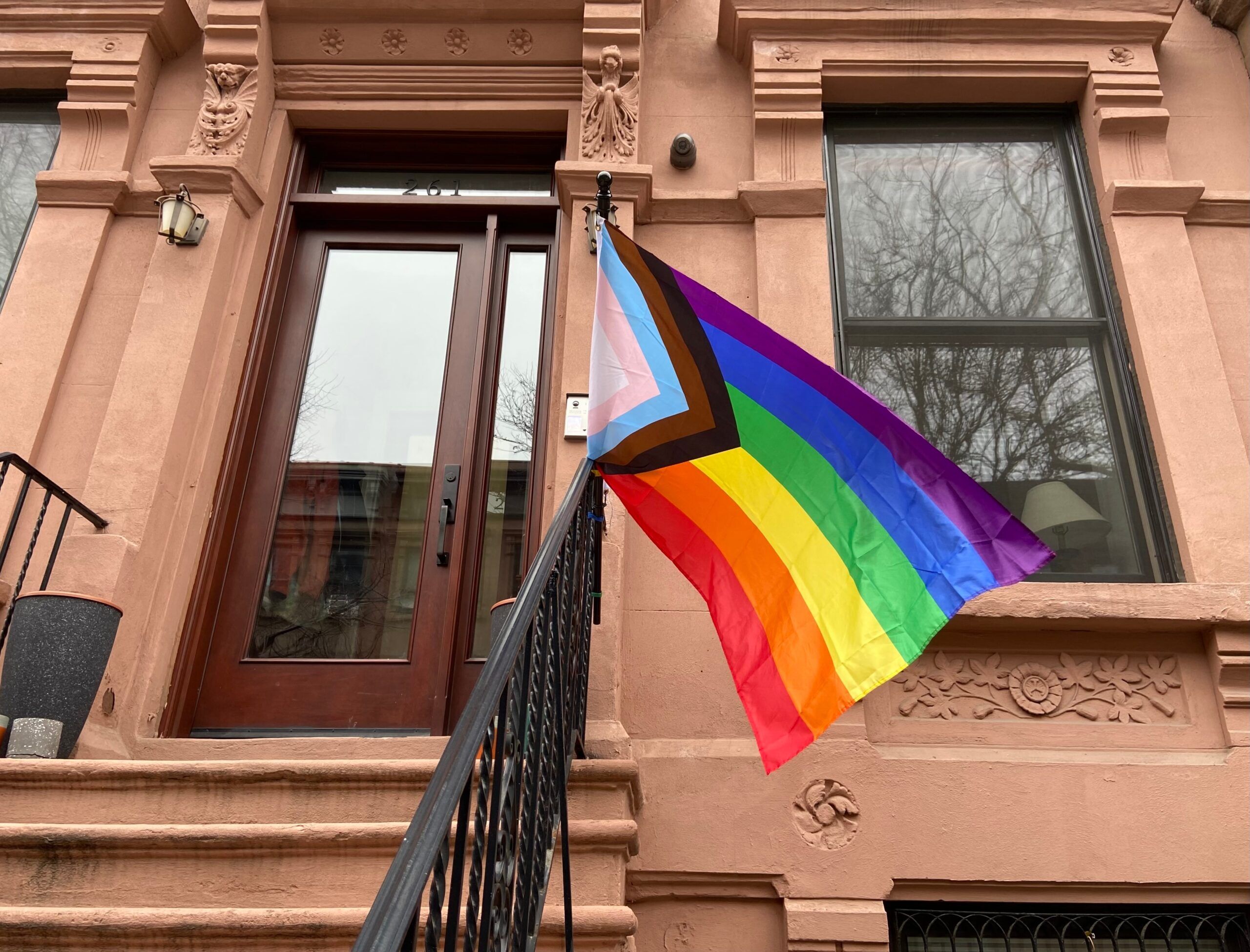 Progress Pride flag hanging from the porch of a brownstone
