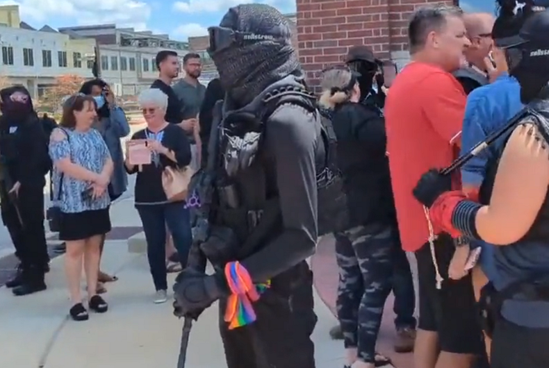 A counterprotestor wears a rainbow while carrying a rifle.
