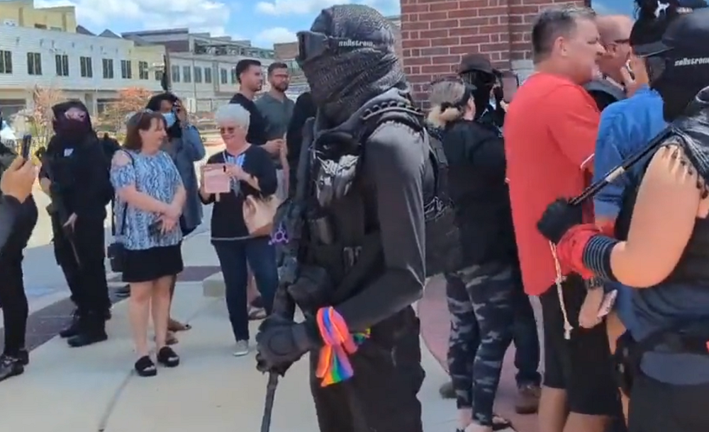 A counterprotestor wears a rainbow while carrying a rifle.