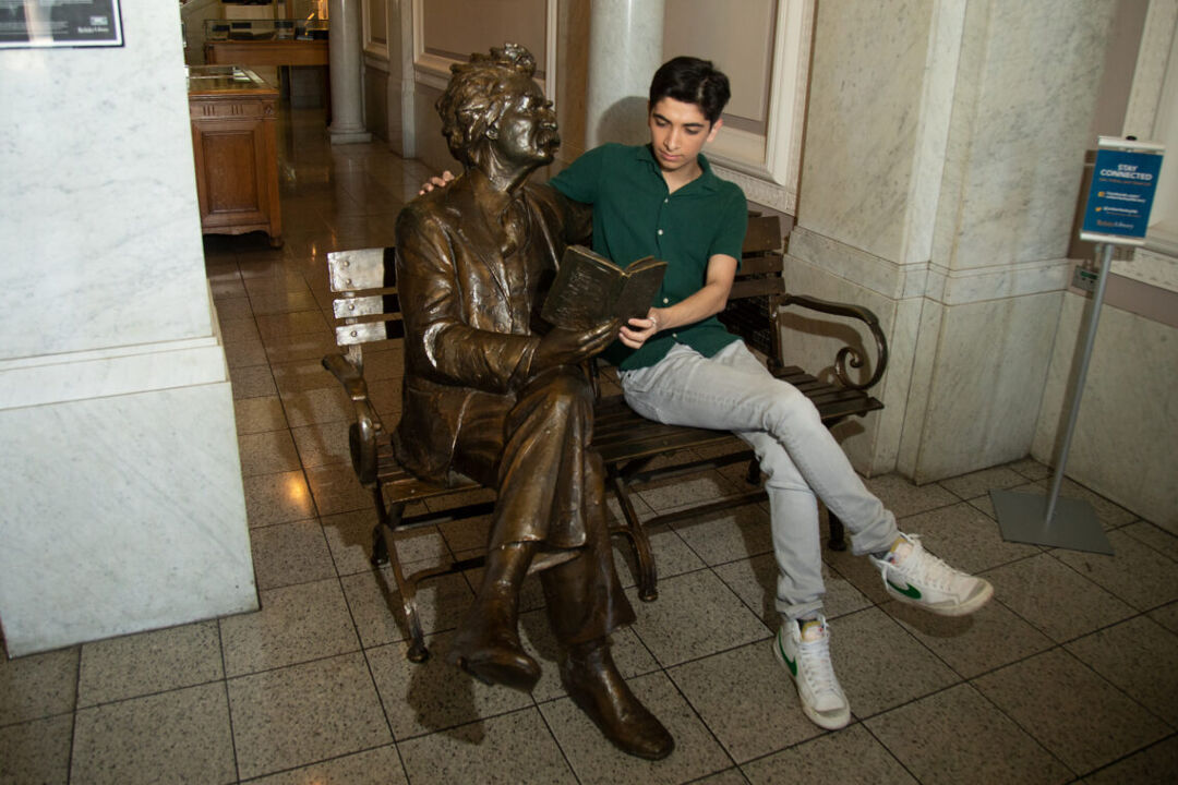 Joseph Arujo takes a moment with Gary Lee Price’s sculpture of Mark Twain at UC Berkeley’s Doe Library. Photo by Marcel Pardo Ariza for LGBTQ Nation