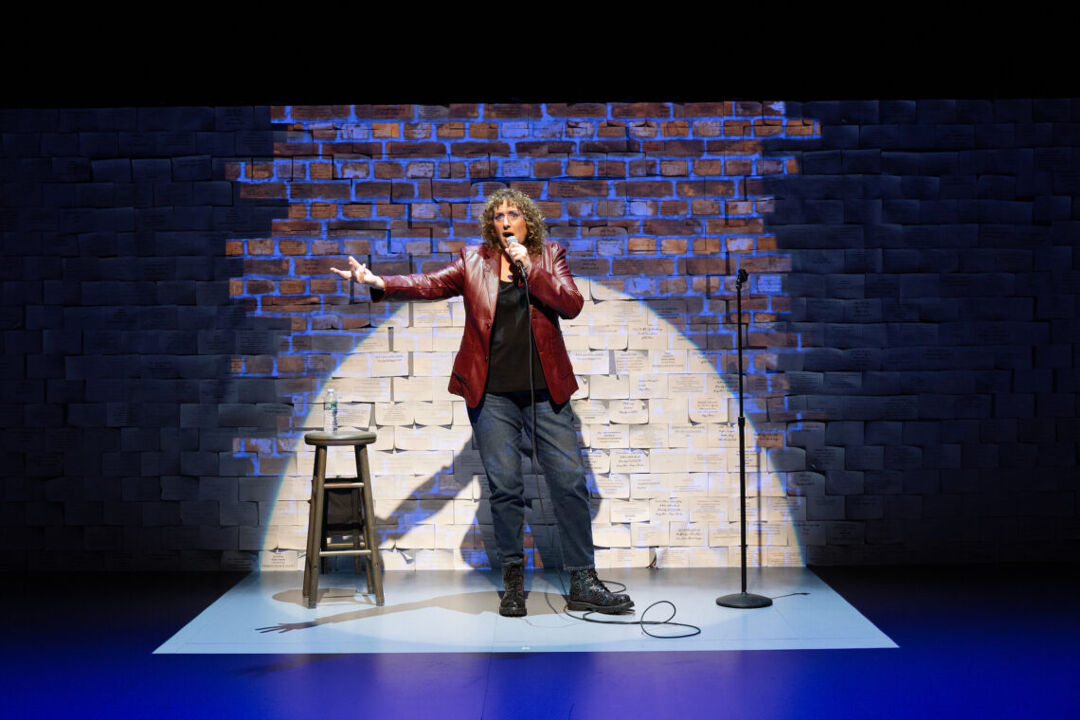 Comedian Judy Gold stands onstage with a mic during her Off-Broadway play Yes, I Can Say That!
