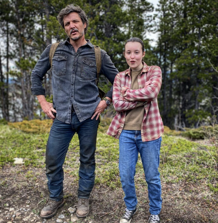 pedro and bella ramsay posing side-by-side in the woods with cute expressions on their faces