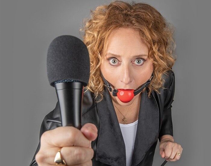Comedian Judy Gold wearing a ball gag and holding a microphone
