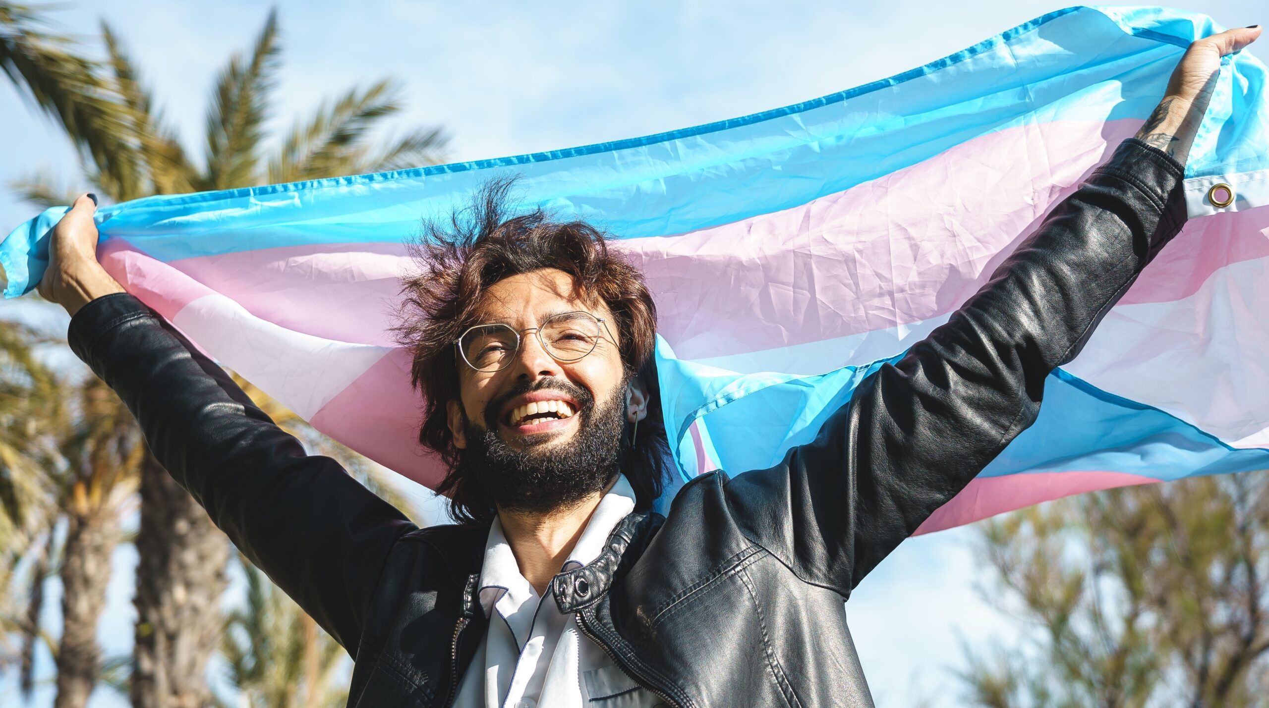 A trans man holds a trans Pride flag
