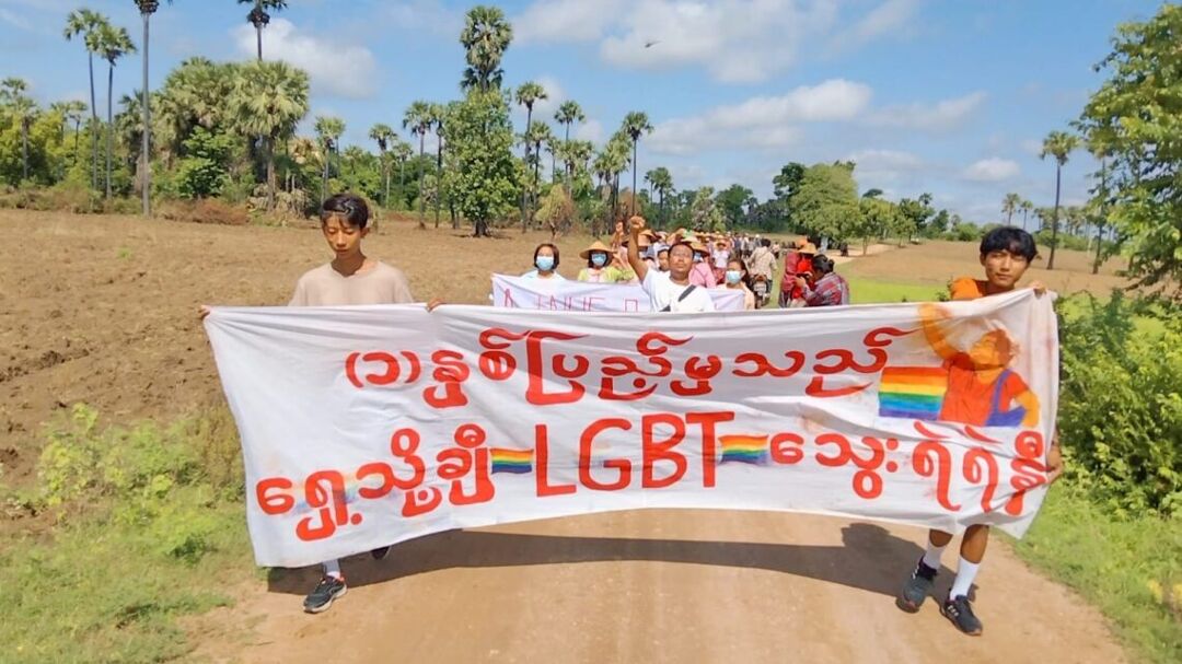 Taken in February 2022, this shows a scene from the daily Yinmabin-Salingyi protest, which brings together various villages from those two townships around copper mines. The banner says "LGBT are Marching Bravely Forward from the First Anniversary (of the revolution)." The figure on the banner depicts a young LGBT protest leader from Yangon. He was in the spotlight after their protest was attacked by security at Myanmar Center shopping center in November 2021. Provided by Thet Oo.