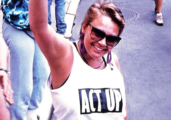 A smiling woman in an Act Up tank raises her fist at the New York Pride parade in 1992.