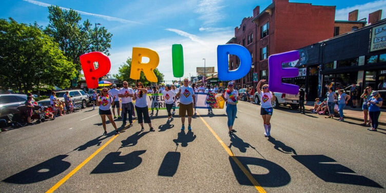 a group of people hold differently colored letter-shaped balloons that spell PRIDE
