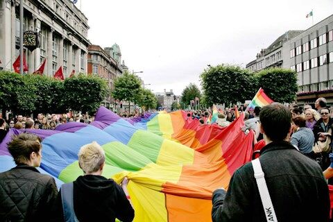 a large rainbow pride flag being marched down a street for Dublin Pride