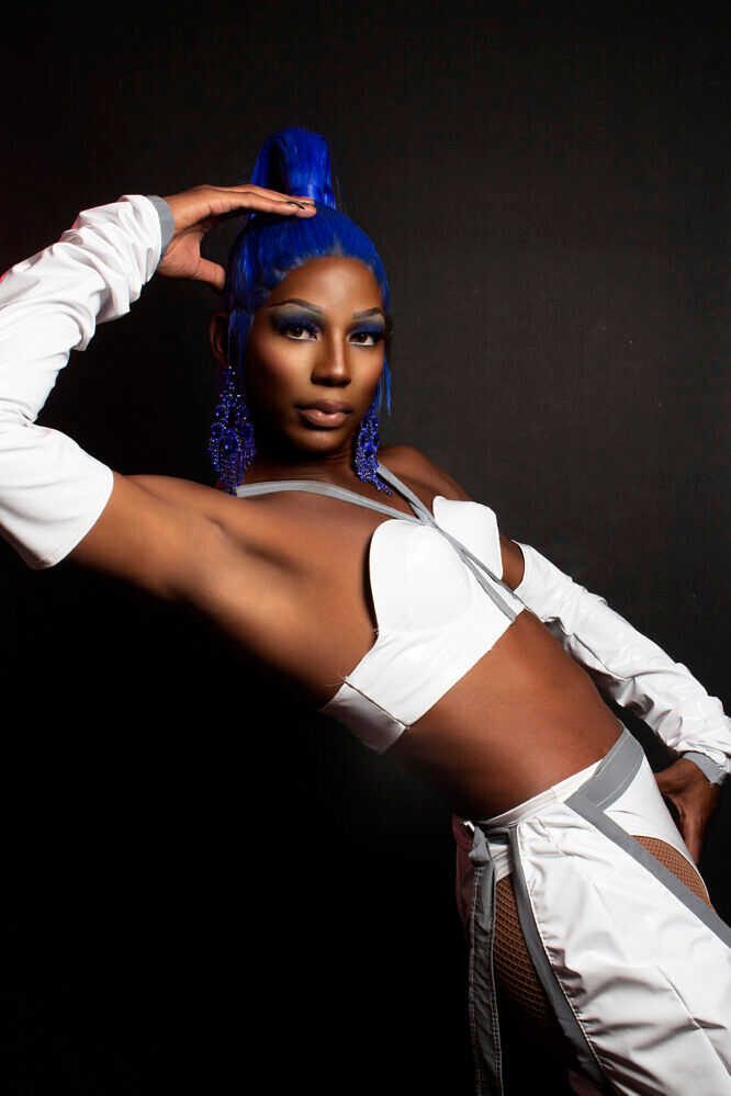 Kyre Jeté the drag queen striking a pose in a white outfit with blue hair and blue earrings