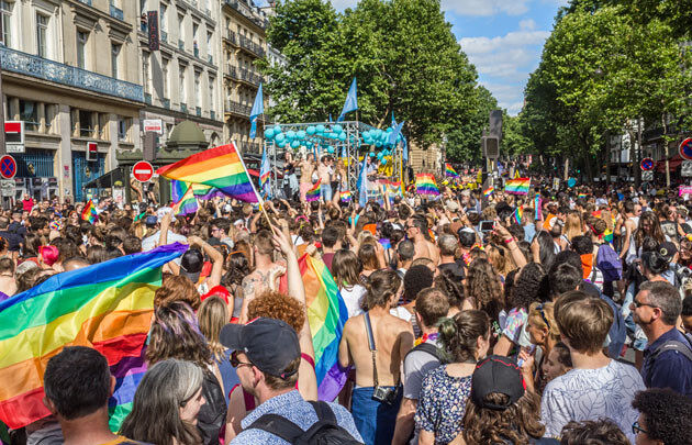 a street in Paris is packed with people celebrating Marche des Fiertés LGBT donned in rainbow flags