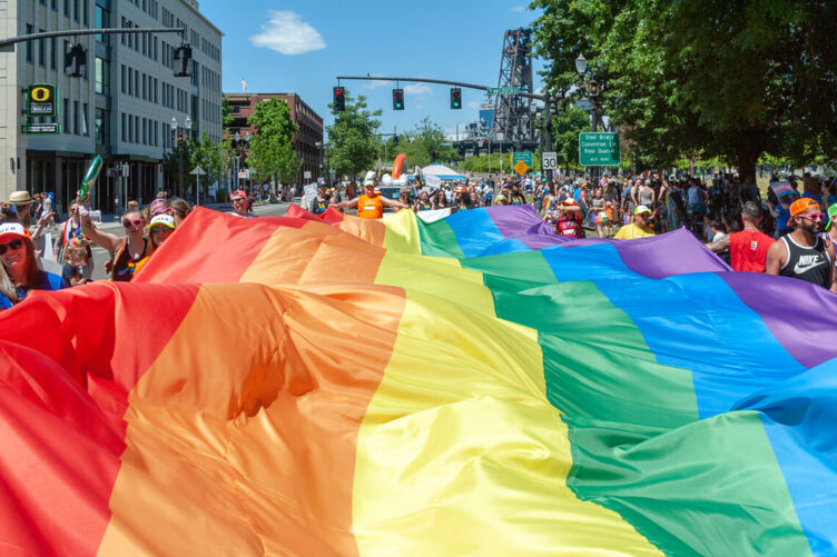 a group of people carry a rainbow pride flag that spans the width of the street in the Portland, OR Pride Parade