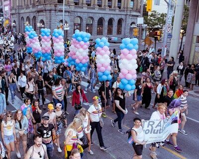 People celebrating Toronto Pride carrying pillars of balloons in the colors of the Trans Flag