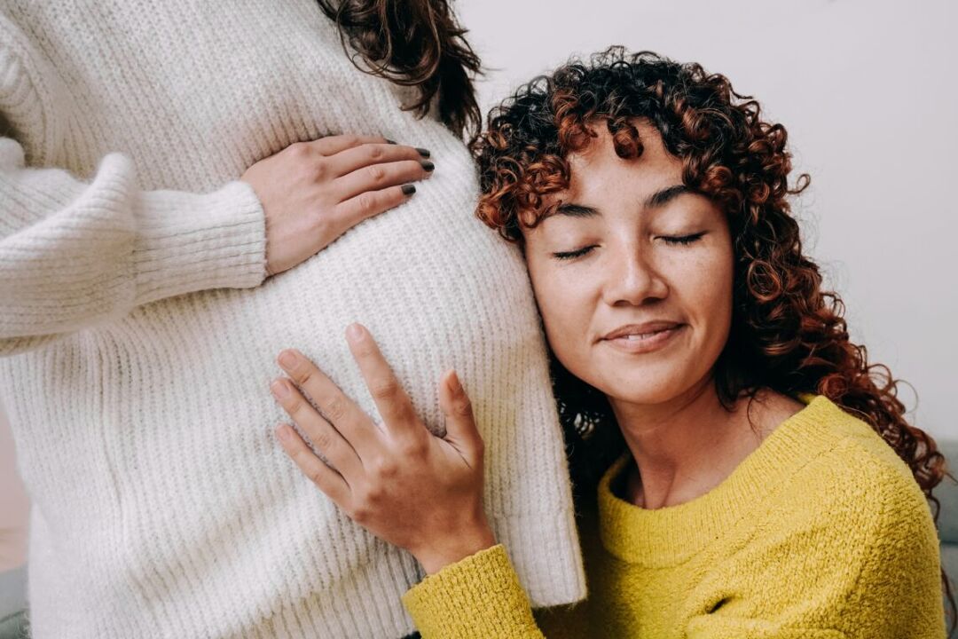LGBT lesbian pregnant woman having tender moment listening her wife baby belly - Focus on right female
