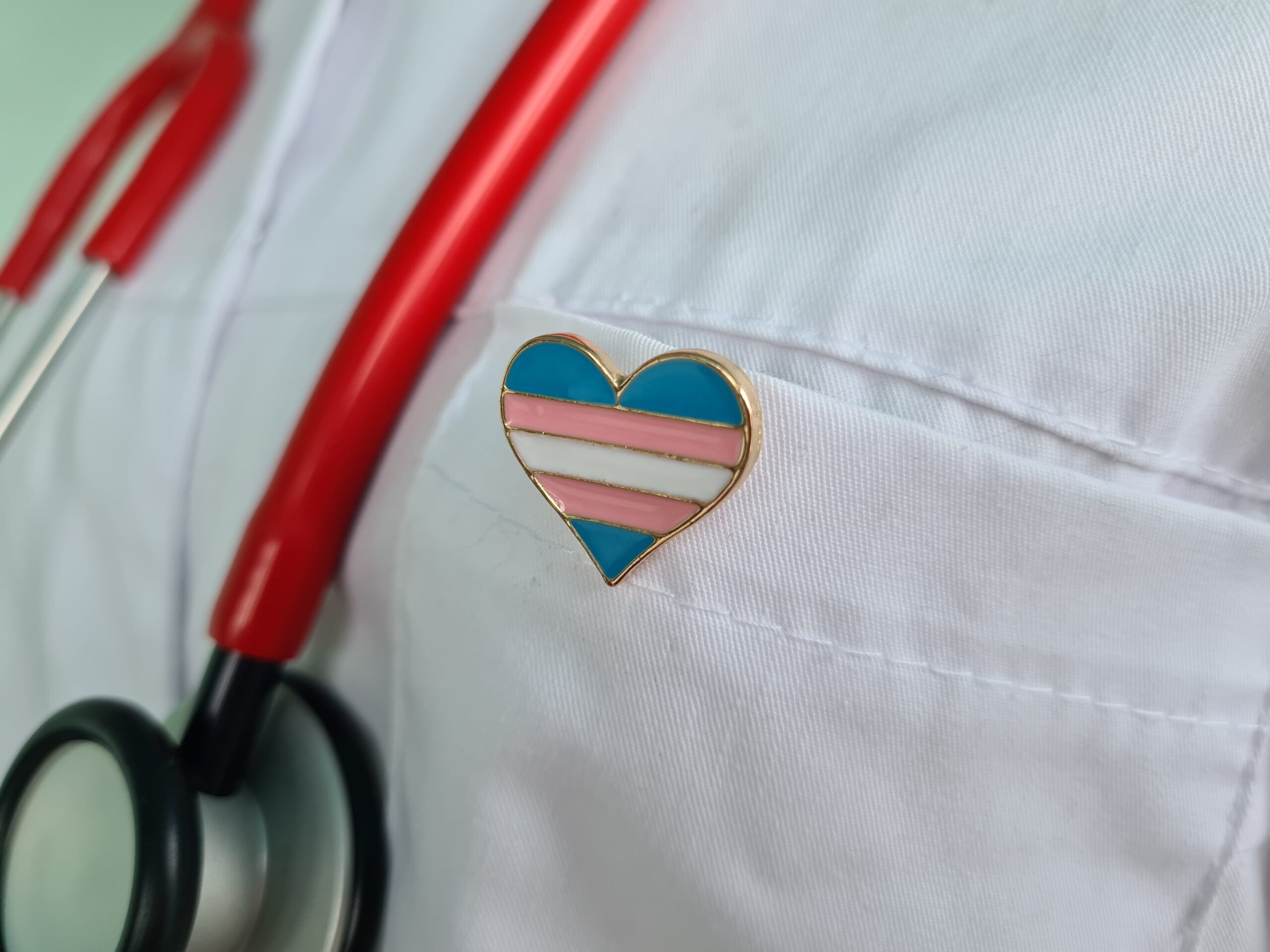Close up of doctor lab coat wearing a stethoscope and heart-shaped trans flag pin