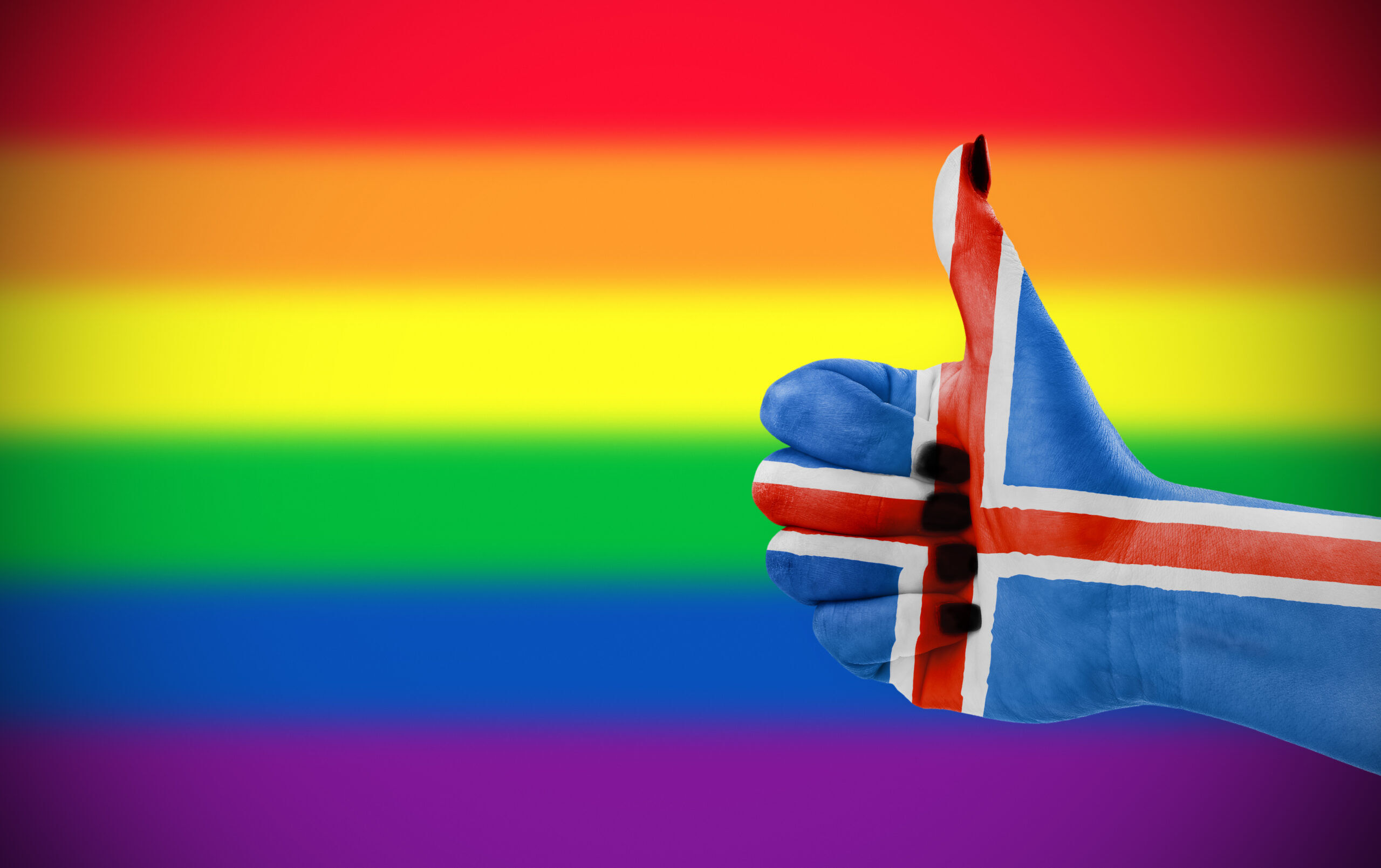 Concept photo - Positive attitude of Iceland for LGBT community. Hand with Icelandic flag painted on it giving thumbs up against rainbow flag. Focus set on hand.