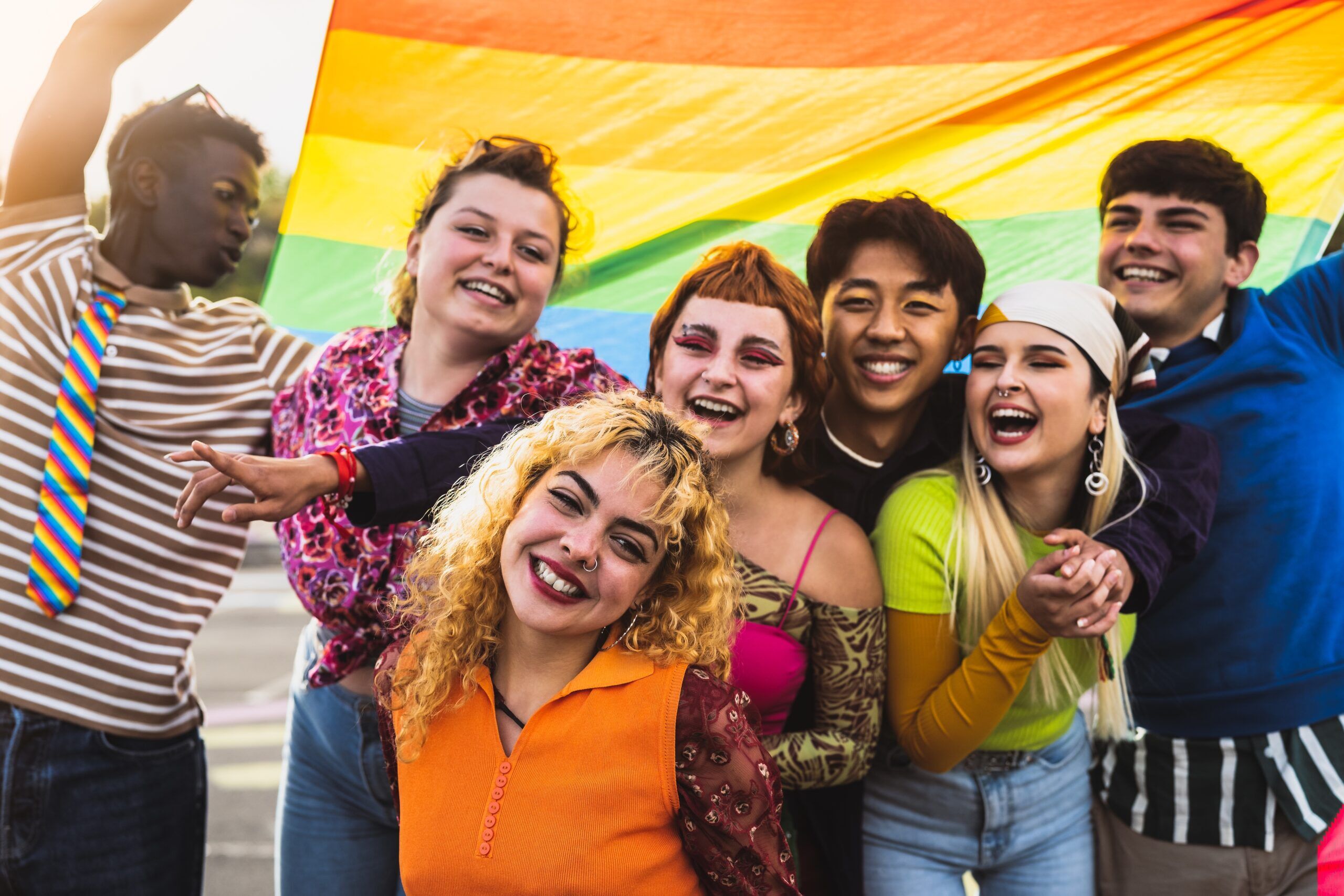 Group of smiling LGBTQ+ people with a rainbow flag