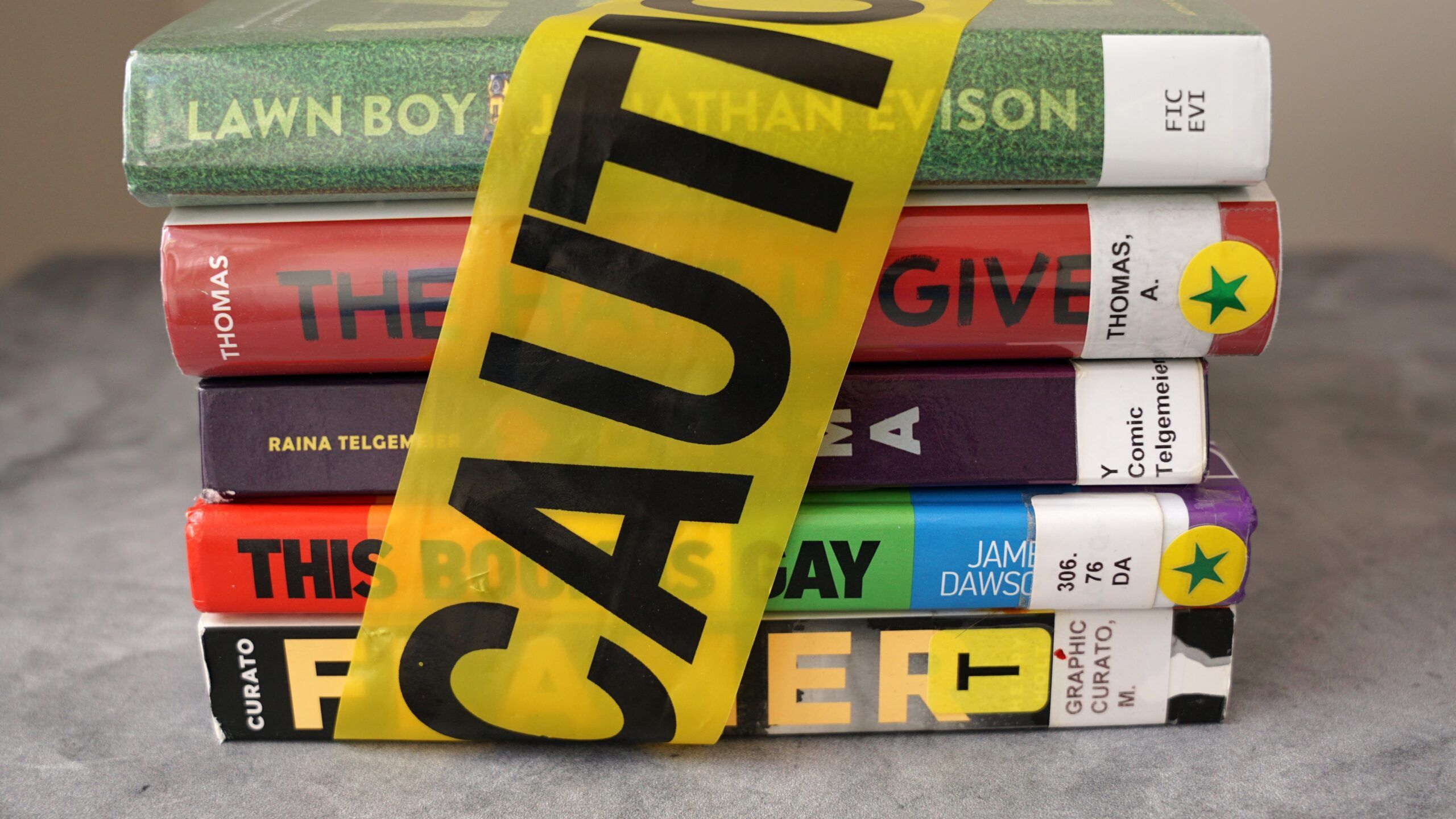 a stack of five banned library books with caution tape wrapped around them
