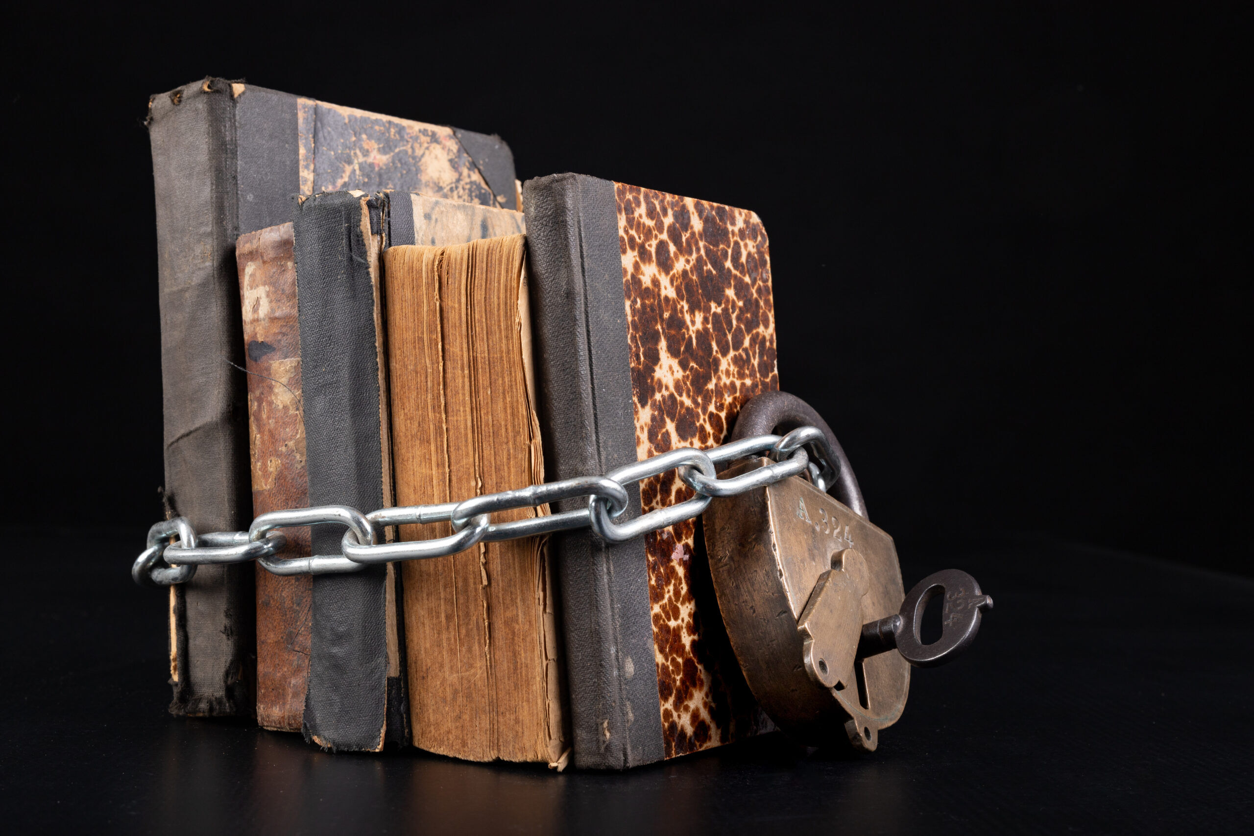 Old books strapping a shiny chain. Forbidden literature locked with a padlock. Dark background.