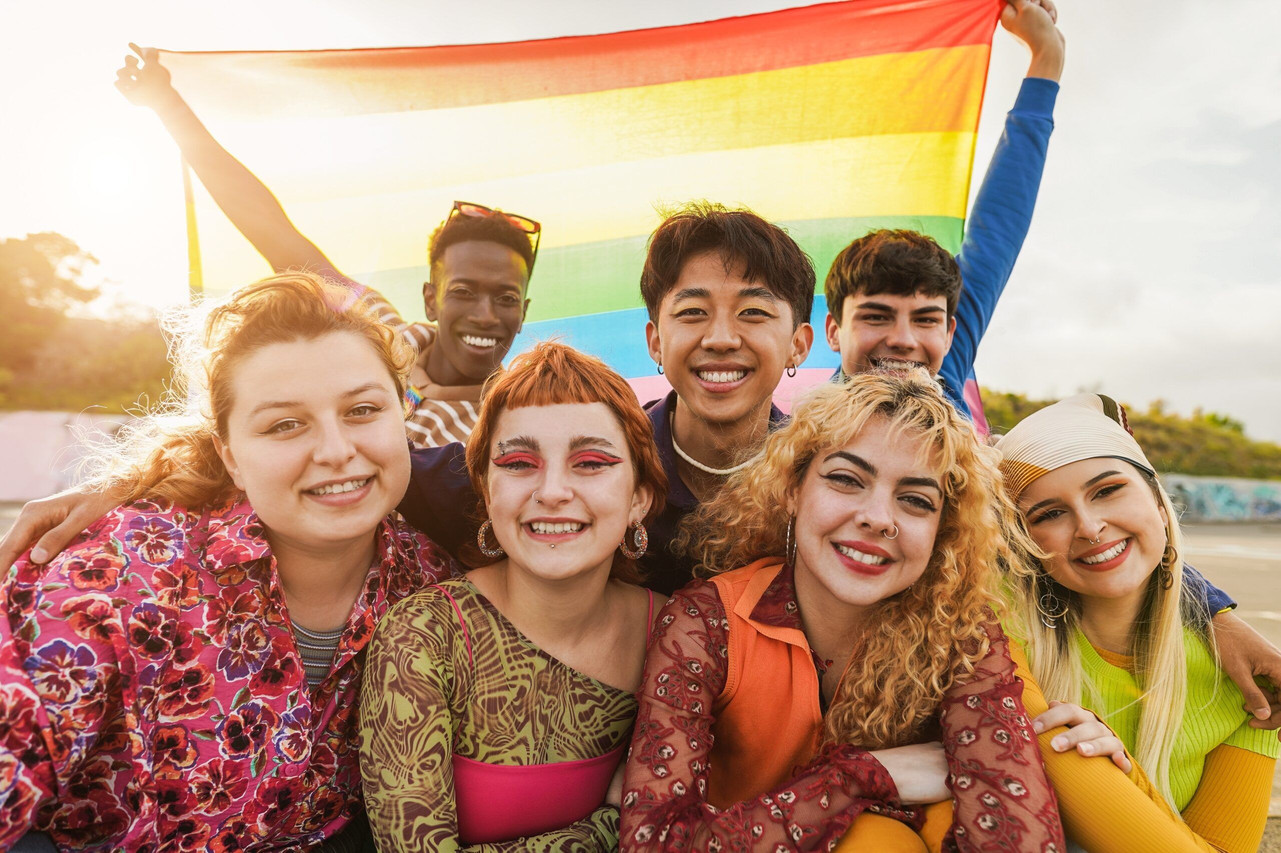 Diverse group of LGBTQ+ youth smiling while holding a rainbow flag