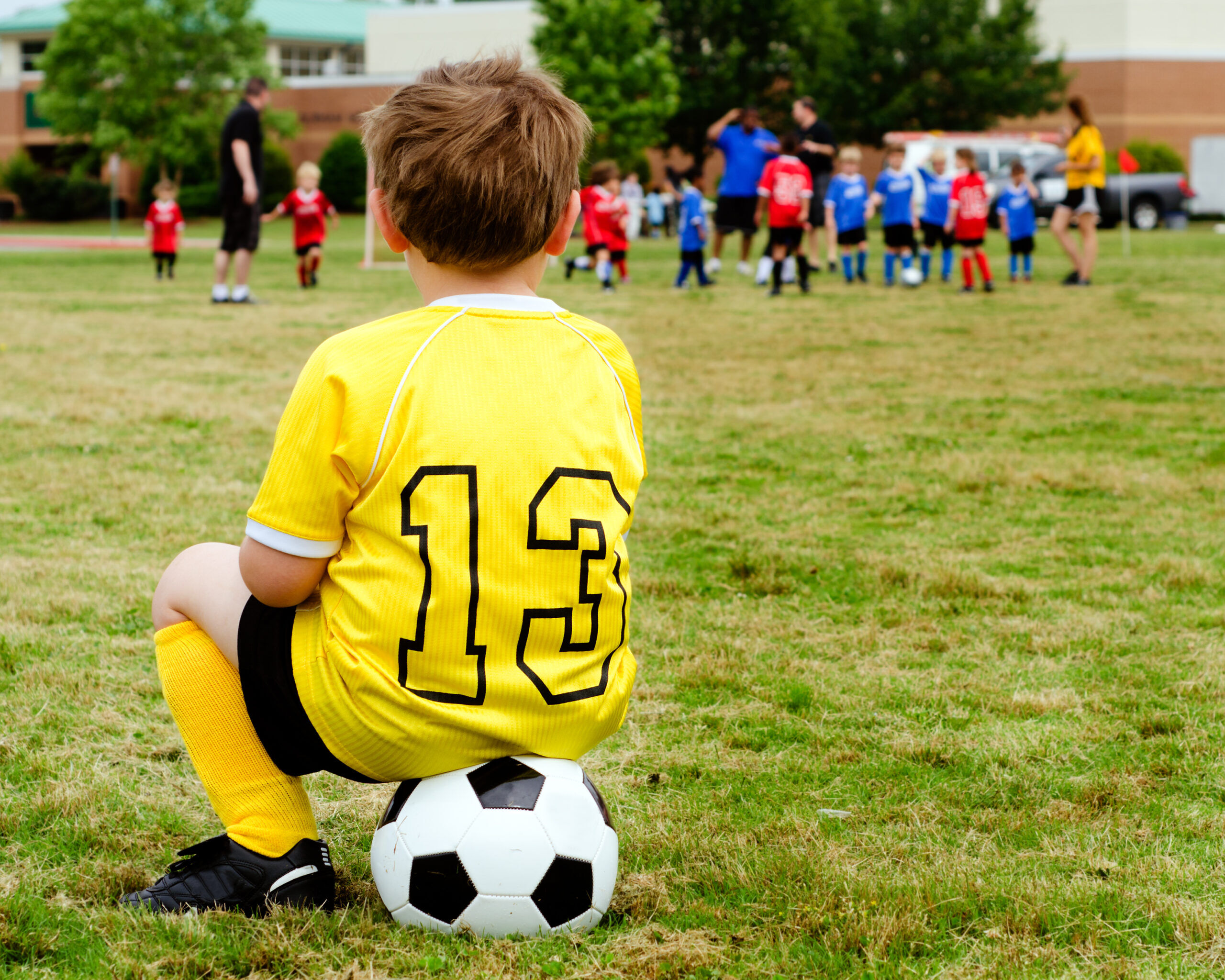 Young boy child in uniform watching organized youth soccer or football game from sidelines