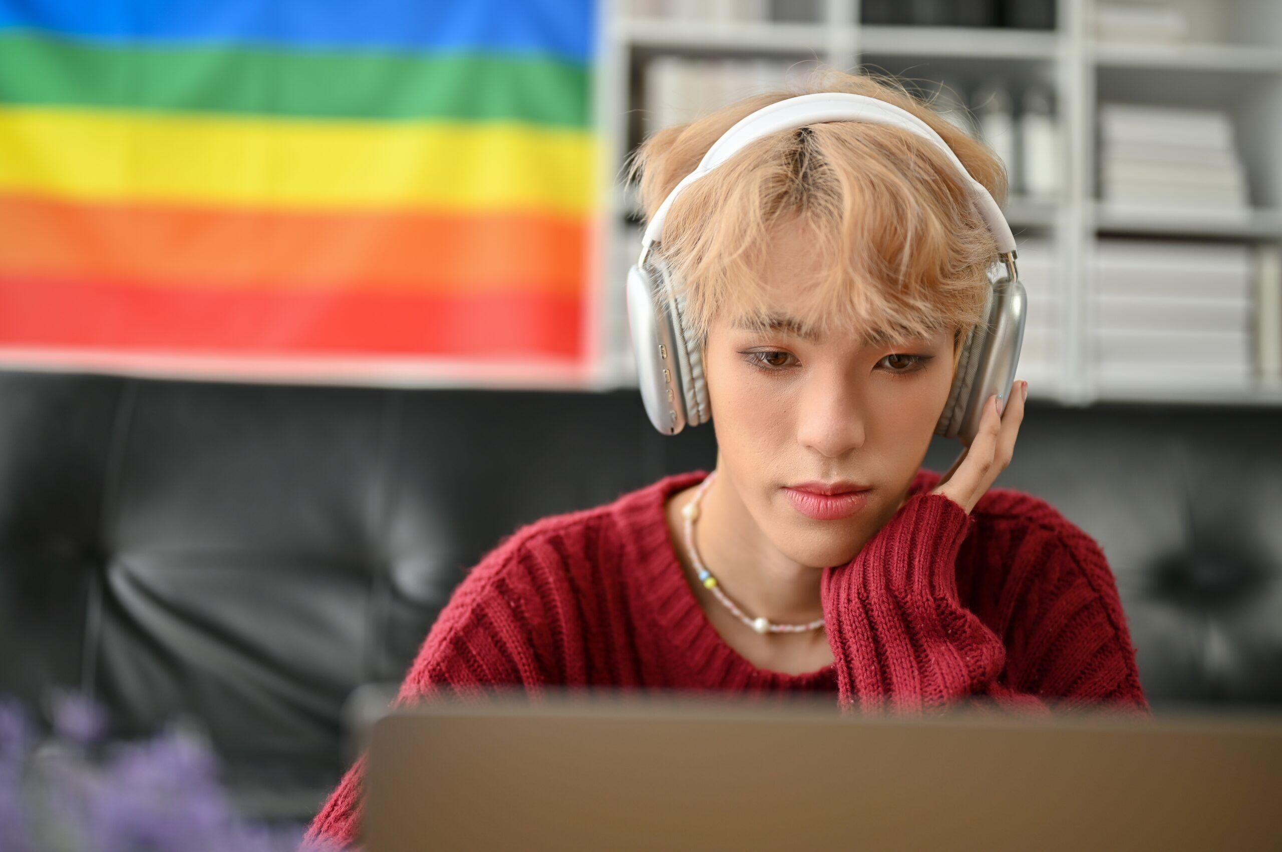 An attractive young Asian gay man focuses on his work on laptop or reads something on a website, looking at his laptop screen, using his laptop computer in the living room.