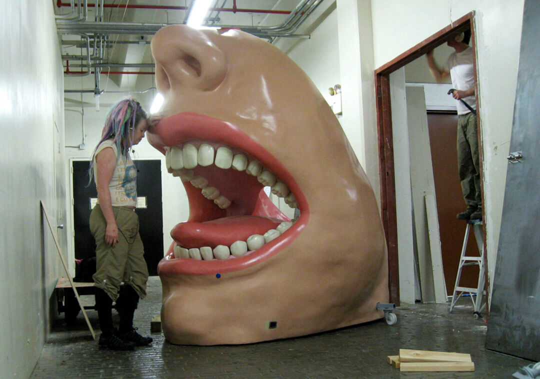 Molly Lenore, left, leans against part of the “Big Mouth” installation at Exploration Place in Wichita, Kansas.