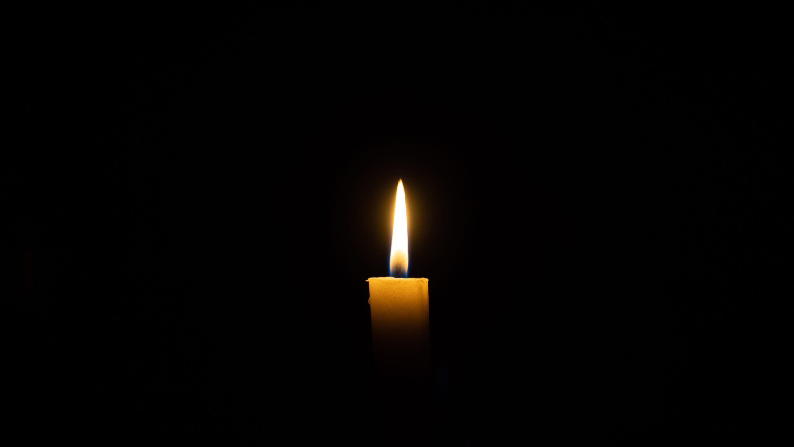 A candle burns in the darkness, copy space. A lit white candle on a black background. Symbol of eternal memory, mourning, minutes of silence, memorial day. The concept of loss and to the memory.