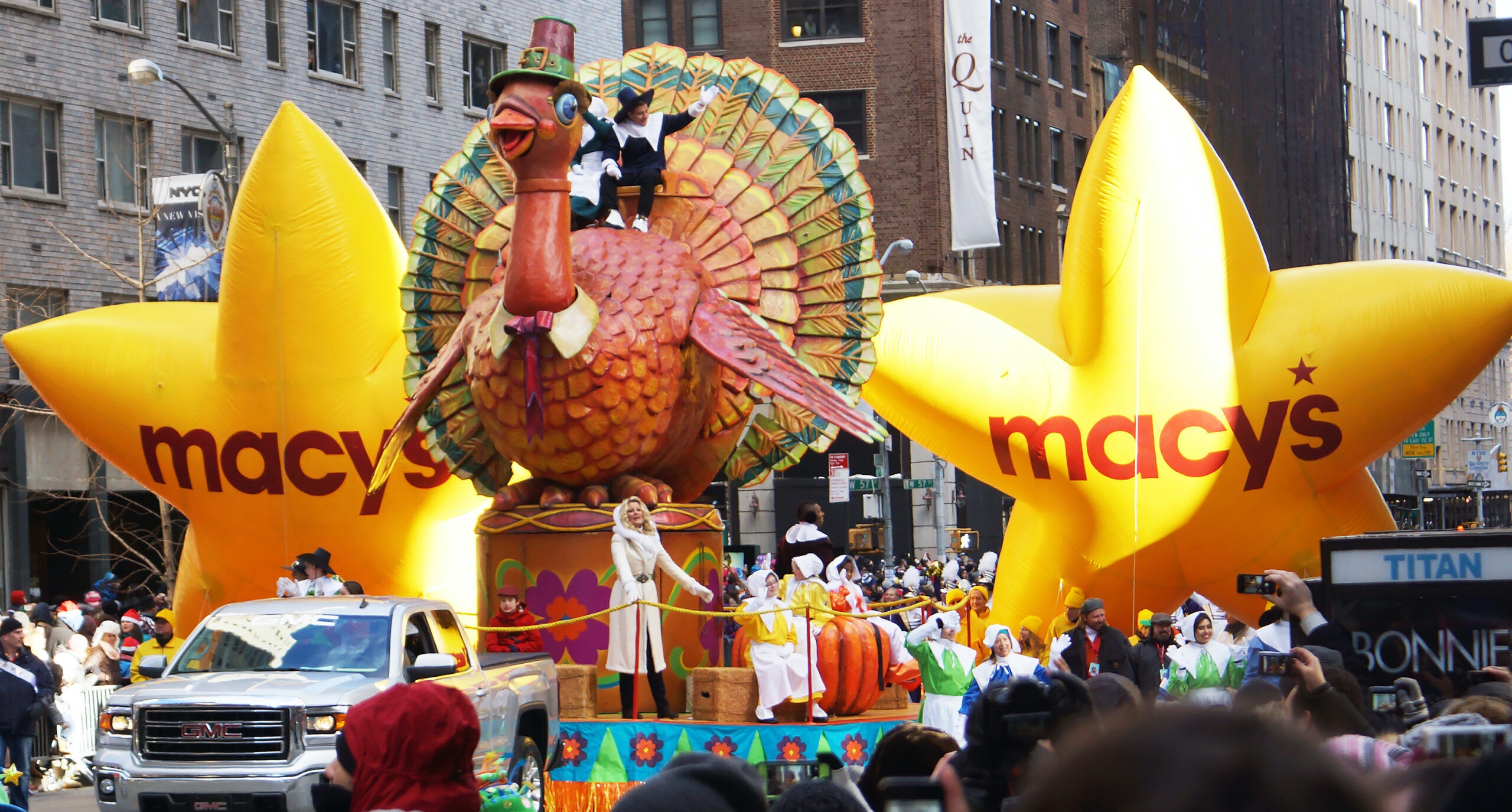 NEW YORK CITY - NOVEMBER 28 2013: the 87th annual Macy's Thanksgiving Day parade attracted hundreds of thousands of spectators. Turkey with Pilgrim riders. Parade marchers are in the streets while large yellow star balloons with Macy's written on them appear next to the large turkey float with a pilgrim riding on top of the bird.
