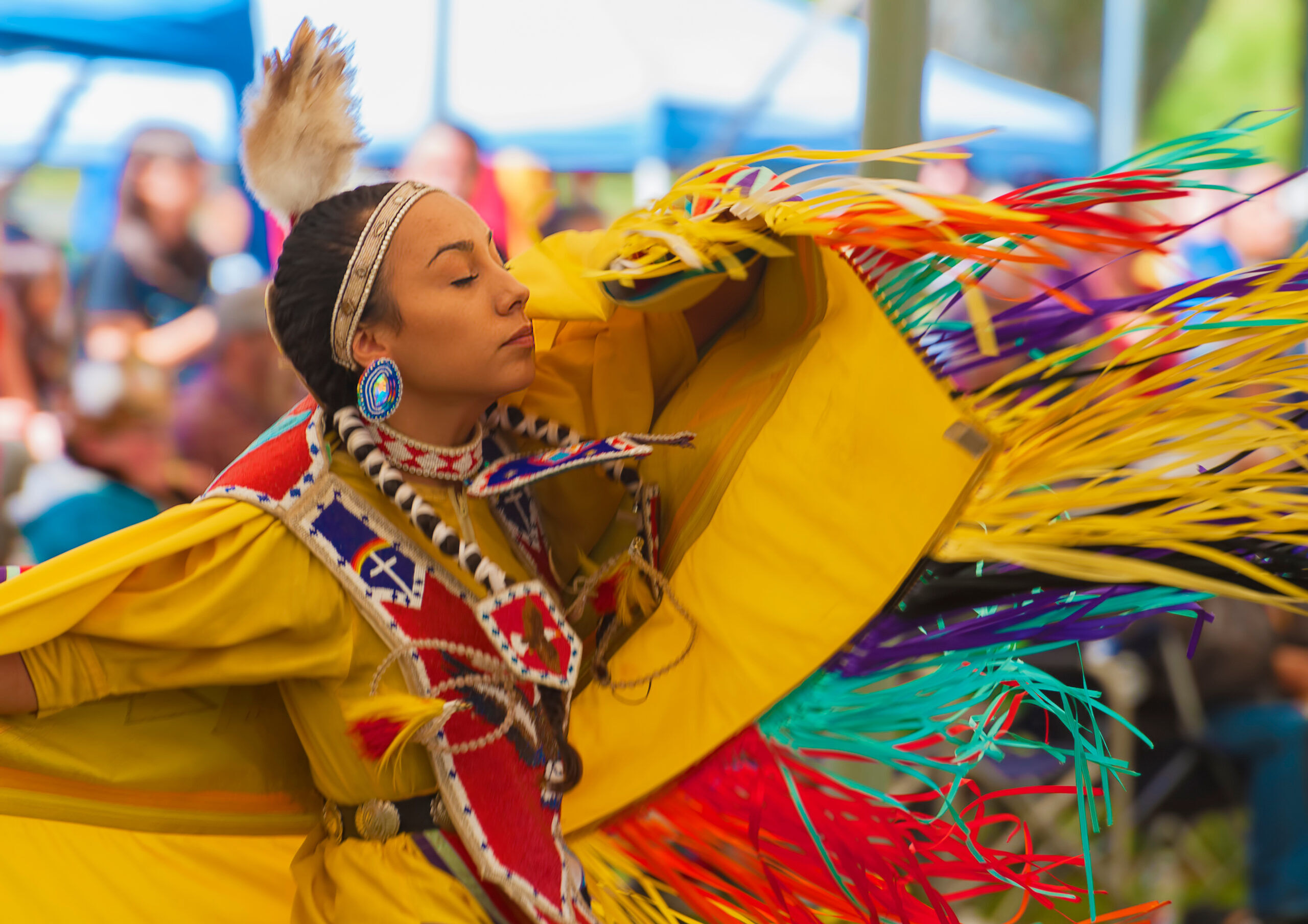 A closeup of a dancing Native American Woman, wearing beaded jewelery, and colorful clothing, while dancing with her eyes closed at the annual Delta Park Pow Wow in Portland, Oregon.