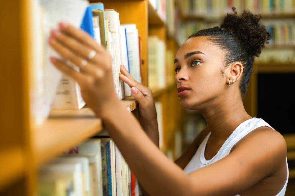 A Black teenager looks at books in her local library.