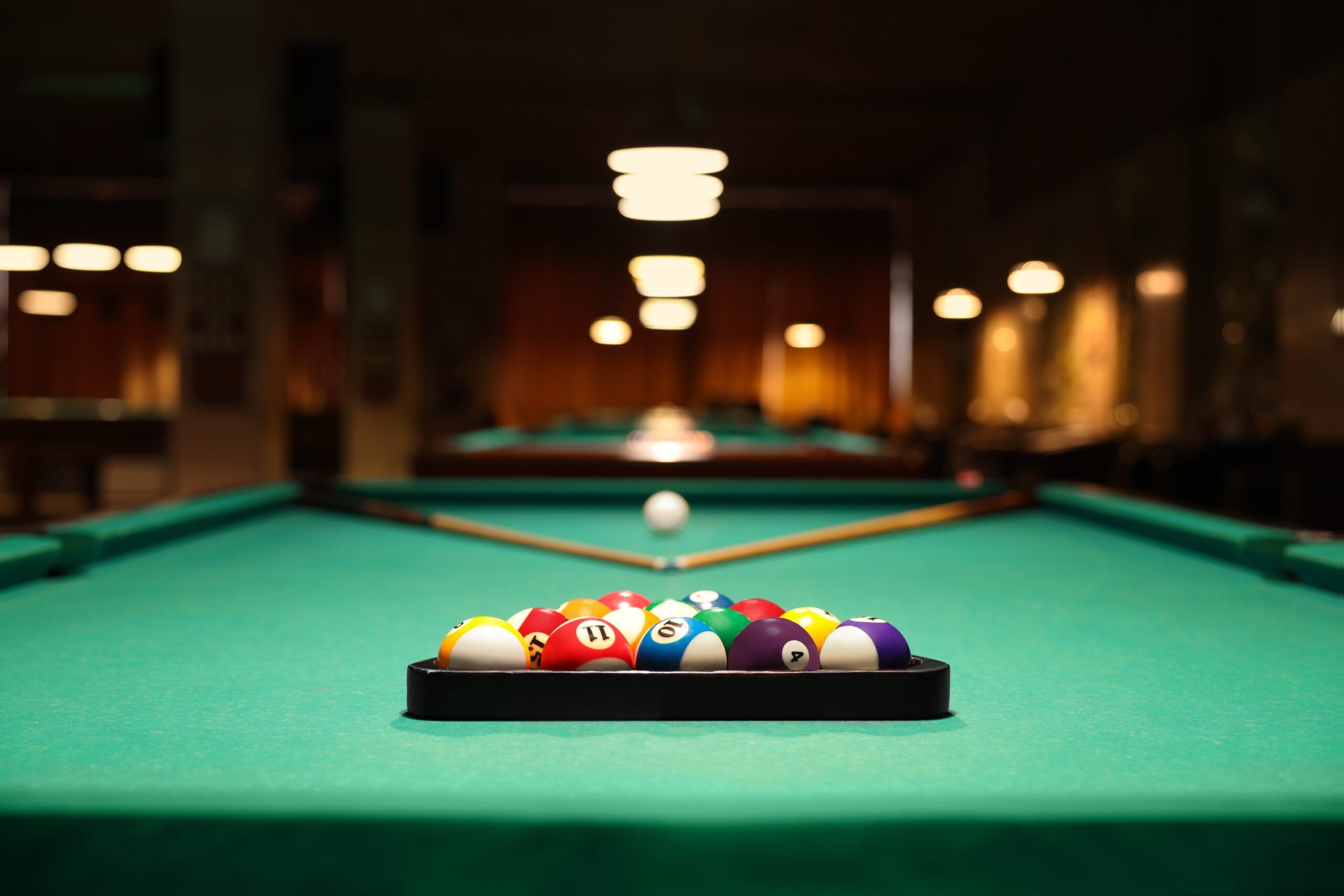 Plastic triangle rack with billiard balls and cues on green table indoors