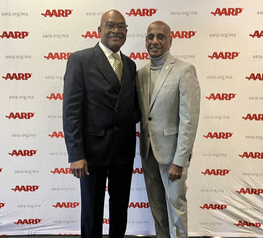 The couple stands in front of a backdrop that says AARP over and over