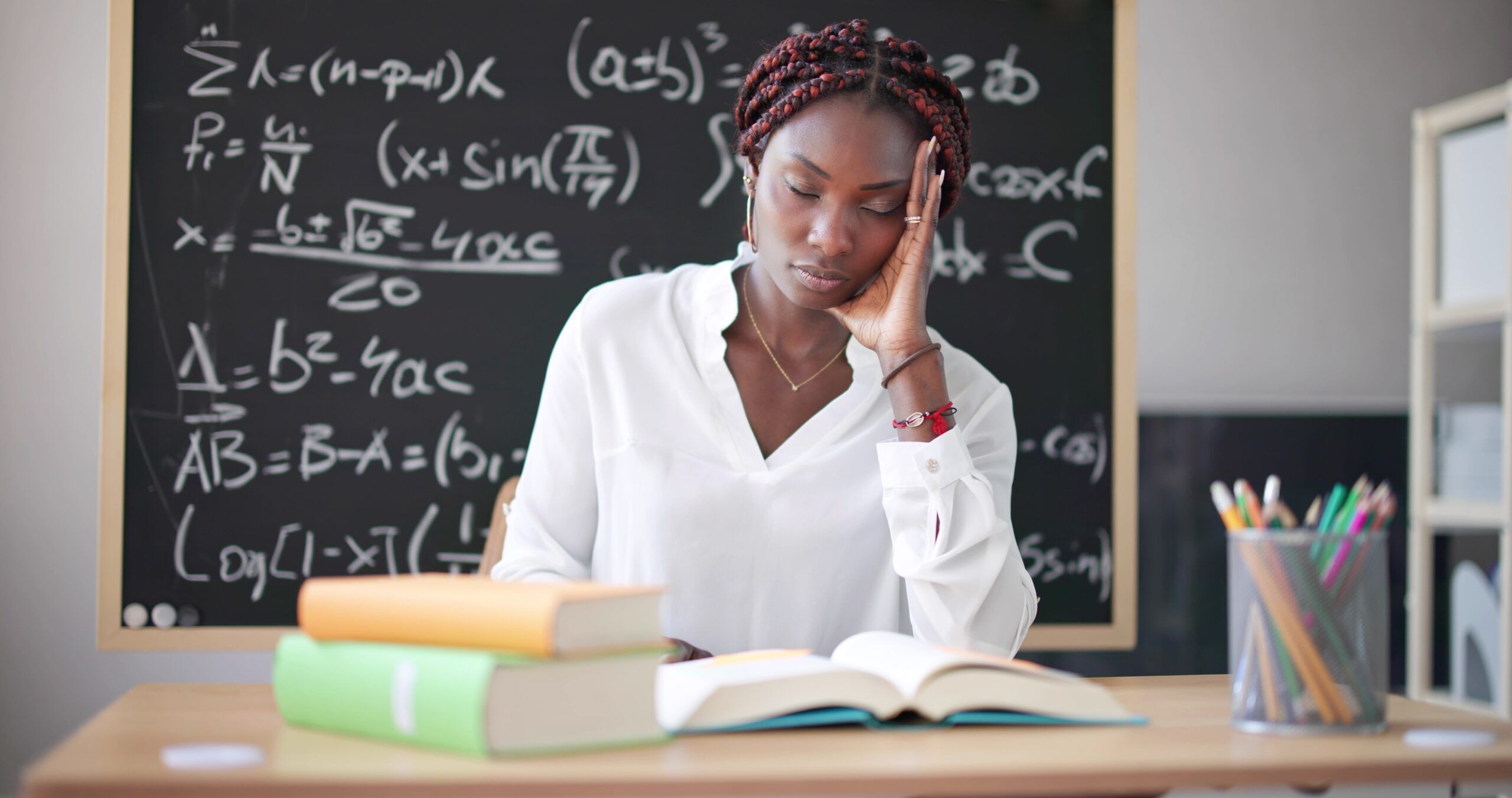 A black math teacher holds the side of her face while feeling stressed out.