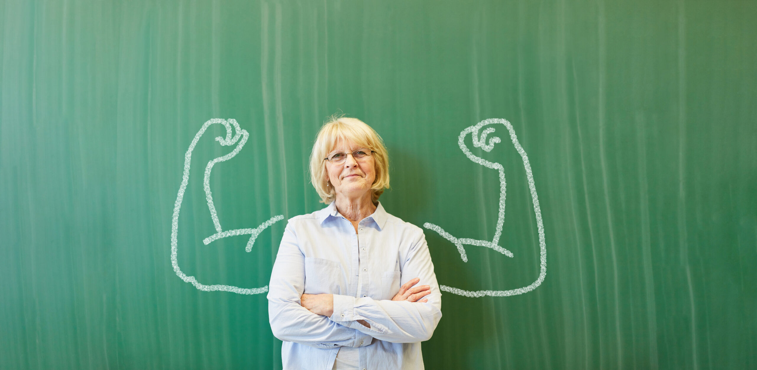 Strong senior teacher with chalk muscles in front of chalkboard