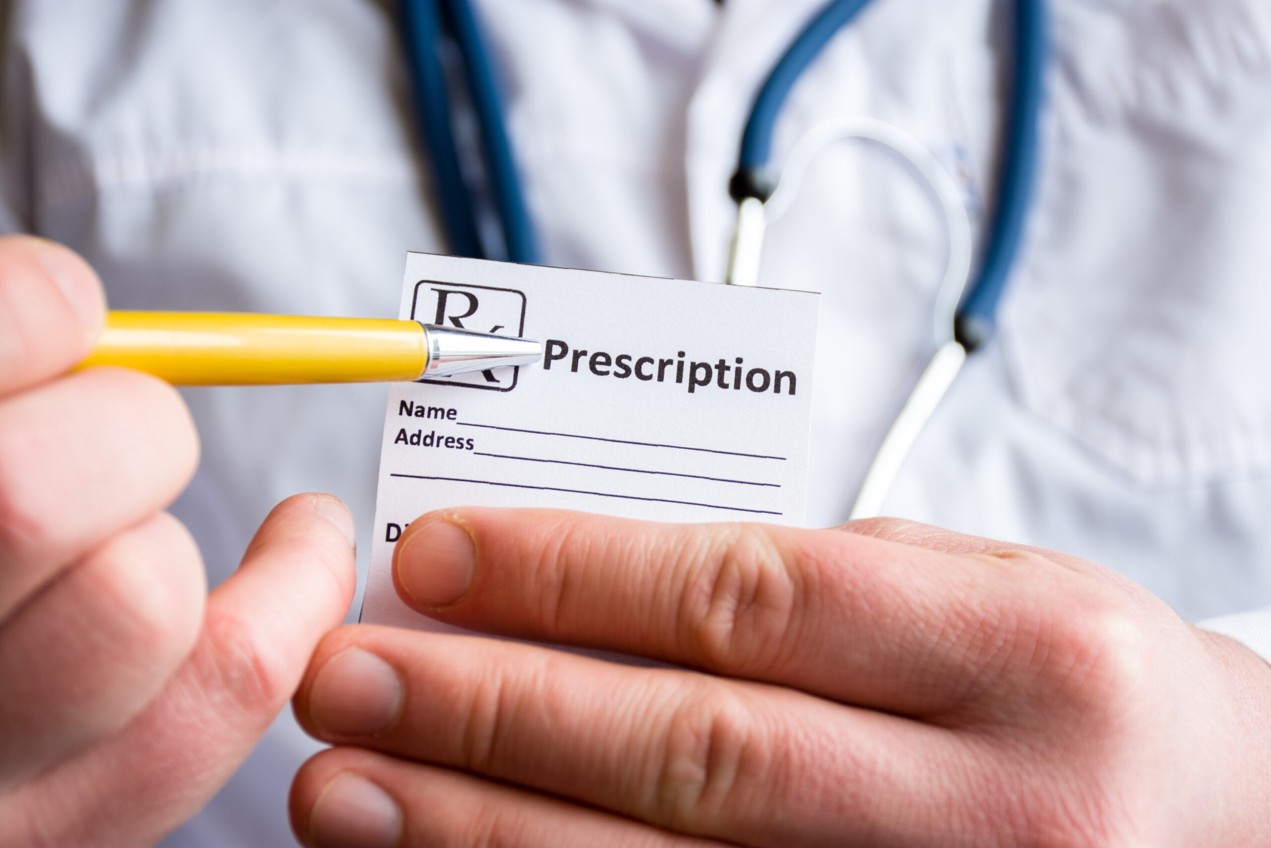 Doctor in foreground holding sample of prescription or recipe for drug, other hand indicates designation of prescription medication, which means issuing medicines by pharmacist only on prescription