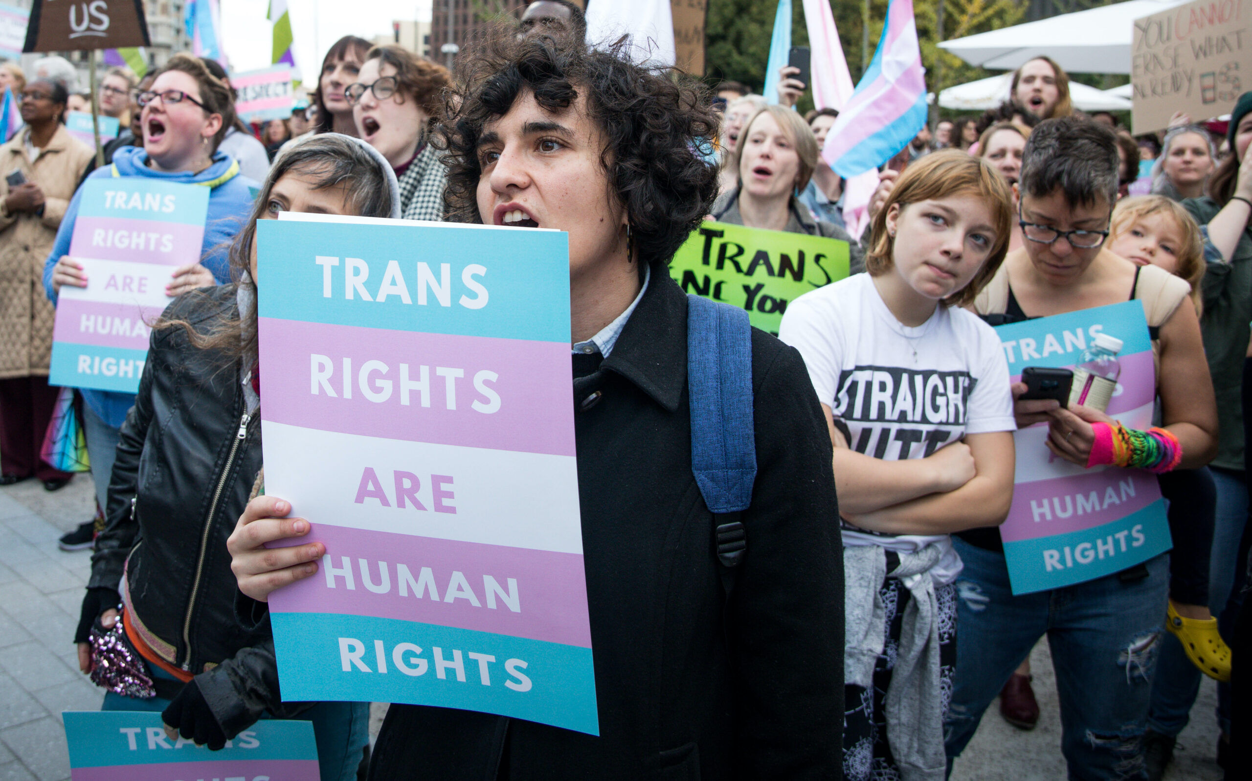 Transgender youths in an outdoor city space hold protest signs declaring that "trans rights are human rights."