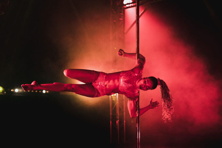 Blackstage Pole performer horizontal on the pole surrounded by smoke and red neon lighting 