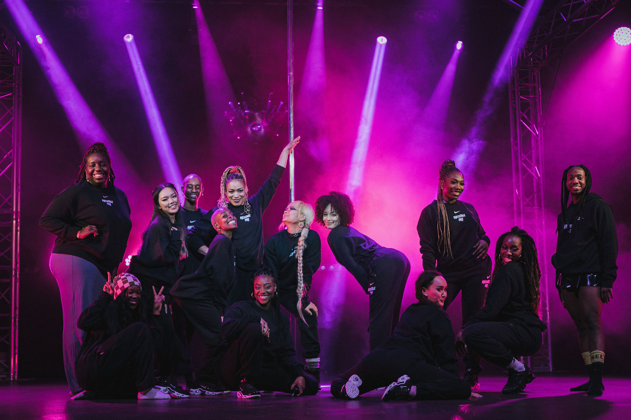 Group of Blackstage Pole performers standing under purple neon lights